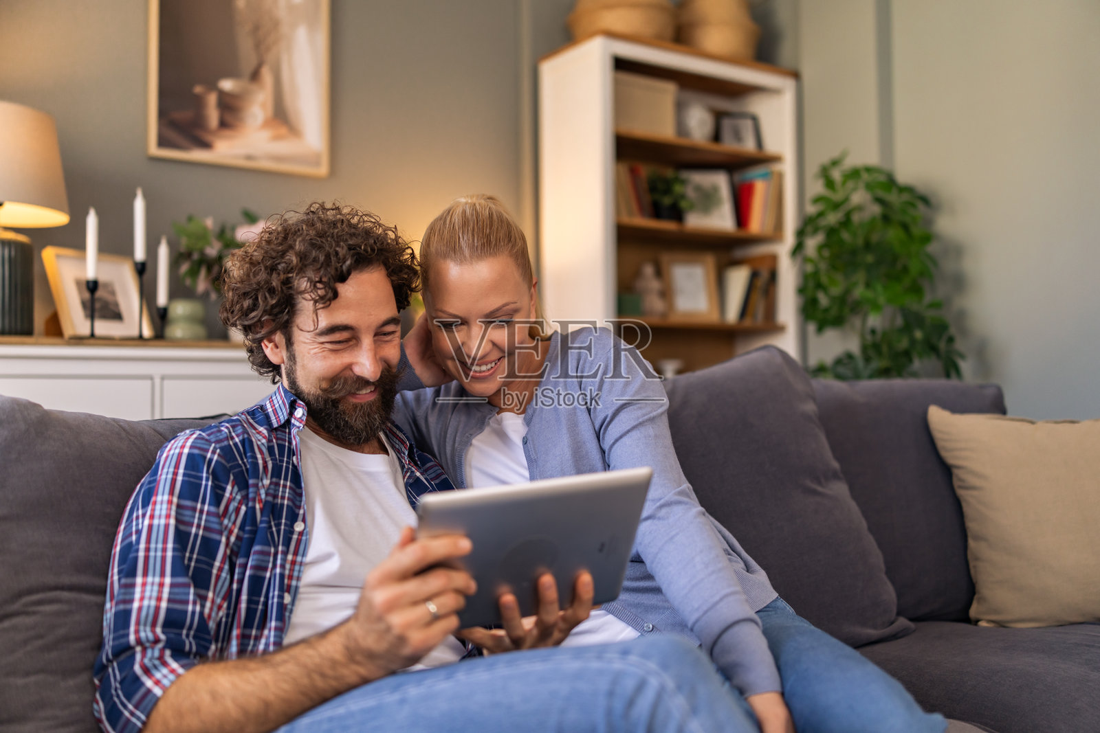 一对情侣在客厅的沙发上依偎在一起，通过平板电脑回顾着他们的过往回忆。照片摄影图片