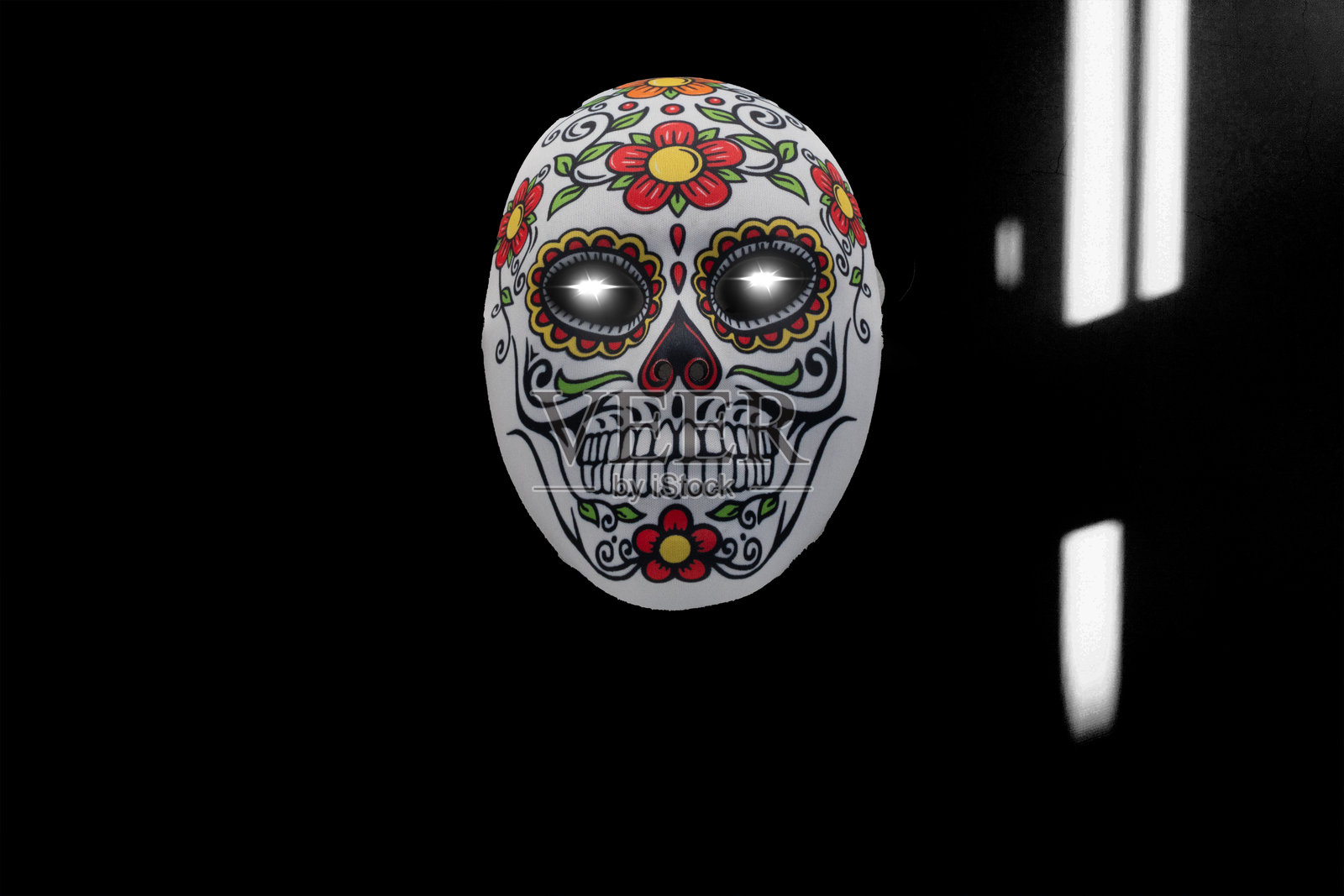 带有传统花卉图案和发光眼睛的骷髅面具，背景为深色照片摄影图片