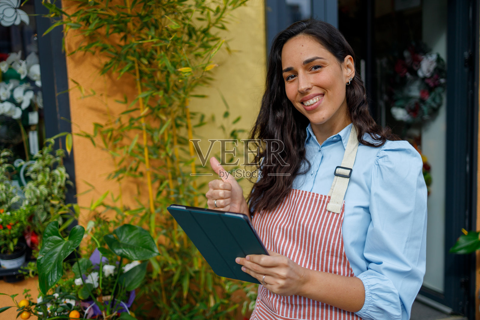 一位面带微笑的女性小企业主，在她的花店外竖起大拇指，手中拿着平板电脑。照片摄影图片