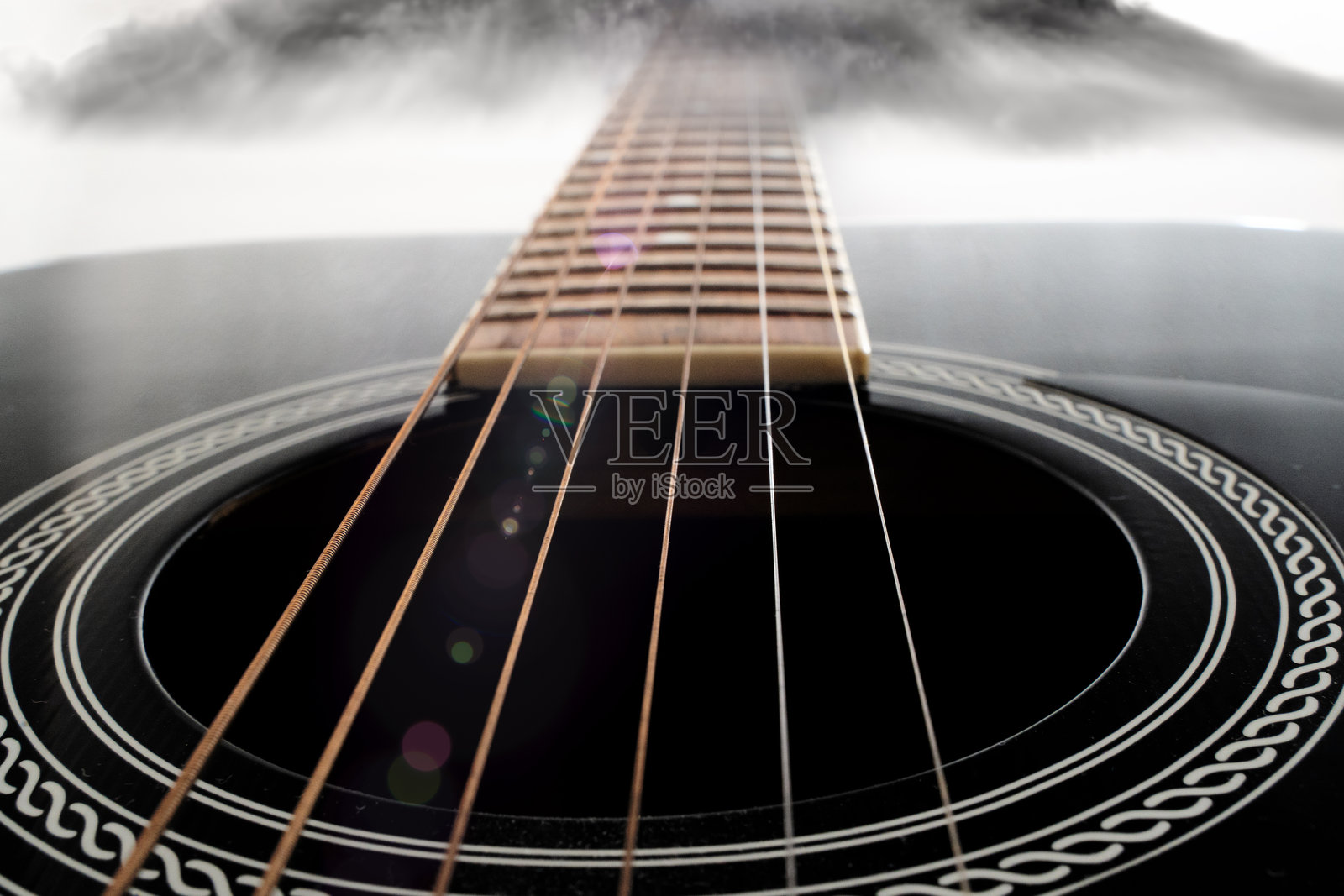 背景有烟雾的声学吉他特写，展示了声音孔上的琴弦照片摄影图片