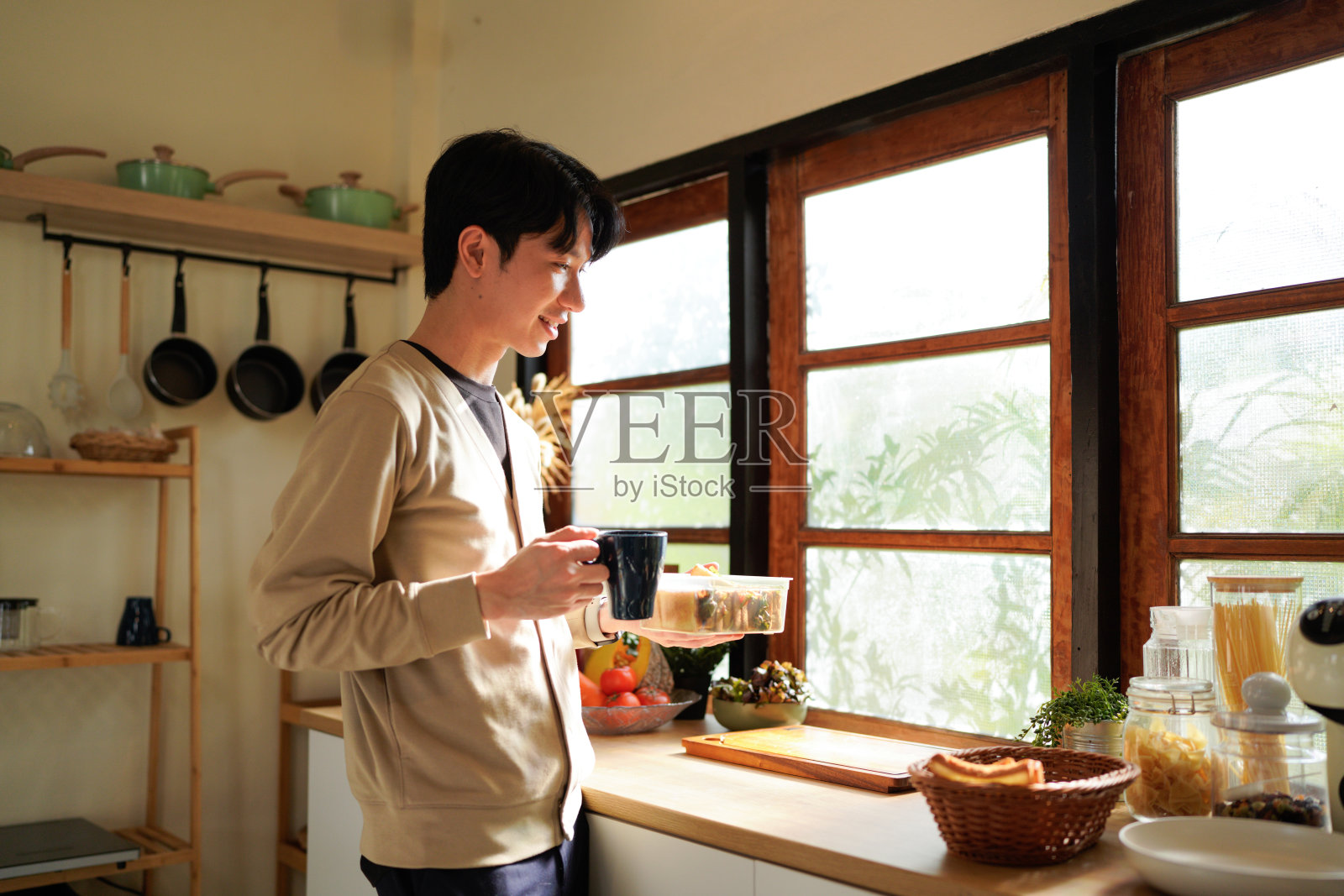 早晨，一个男人在窗边吃三明治喝咖啡，场景轻松随意。照片摄影图片