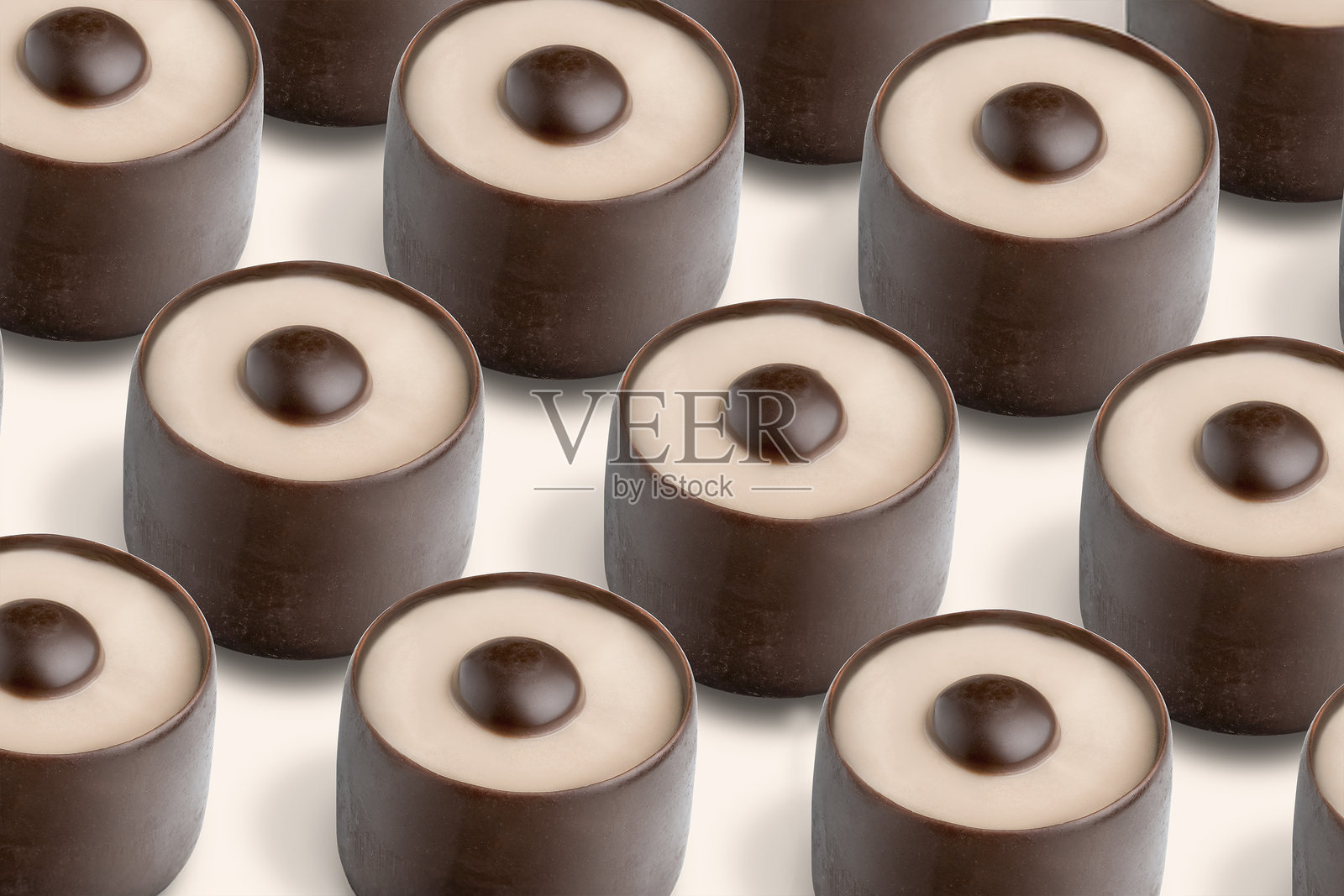 一排排精致的巧克力糖果整齐排列，每一颗都拥有光滑的米色外层和黑巧克力夹心。这些甜点组成了一幅诱人的甜品展示。照片摄影图片