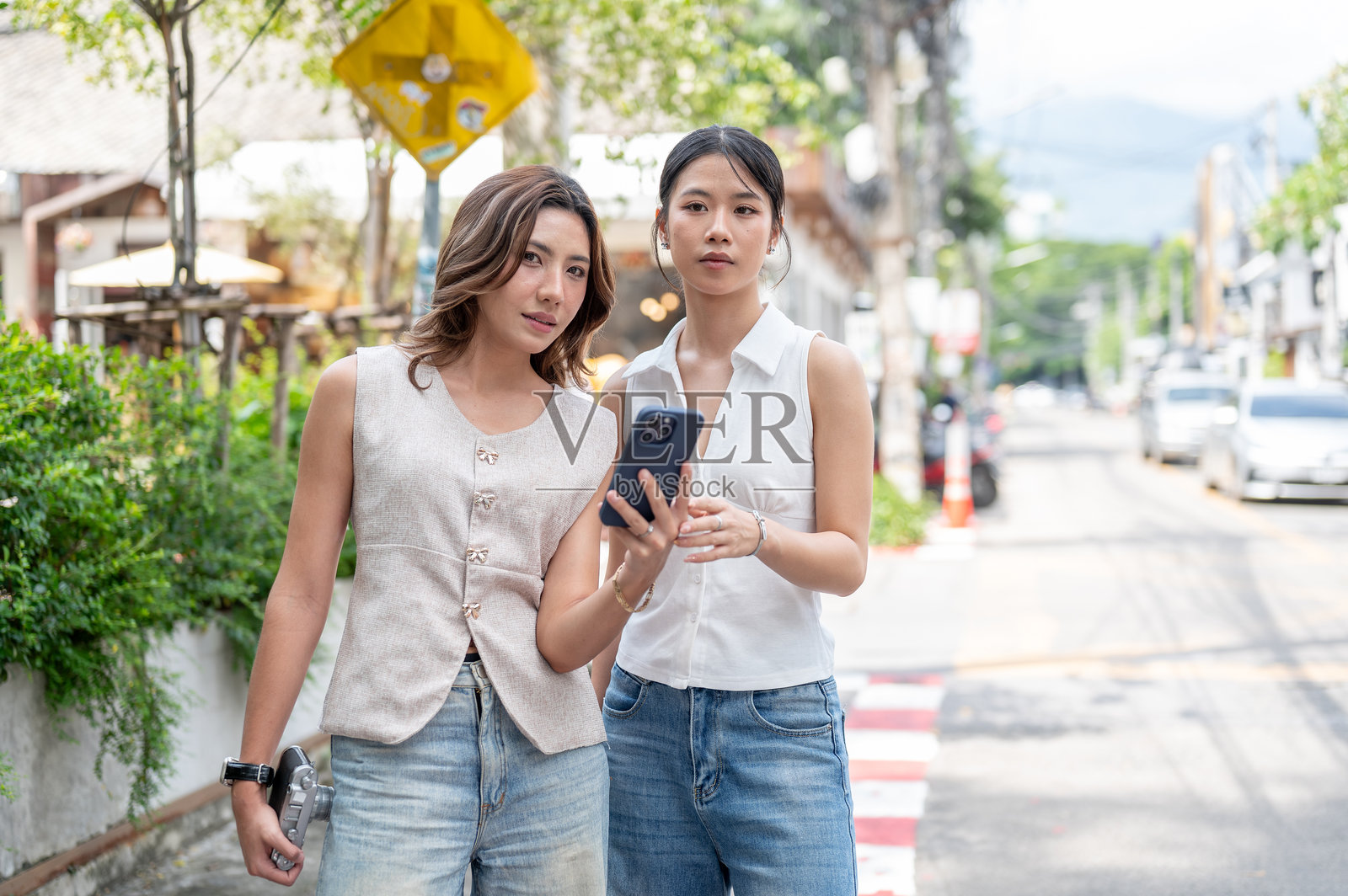 一名亚洲女子站在街边，和朋友一起，她正拿着手机查看地图或呼叫出租车。照片摄影图片