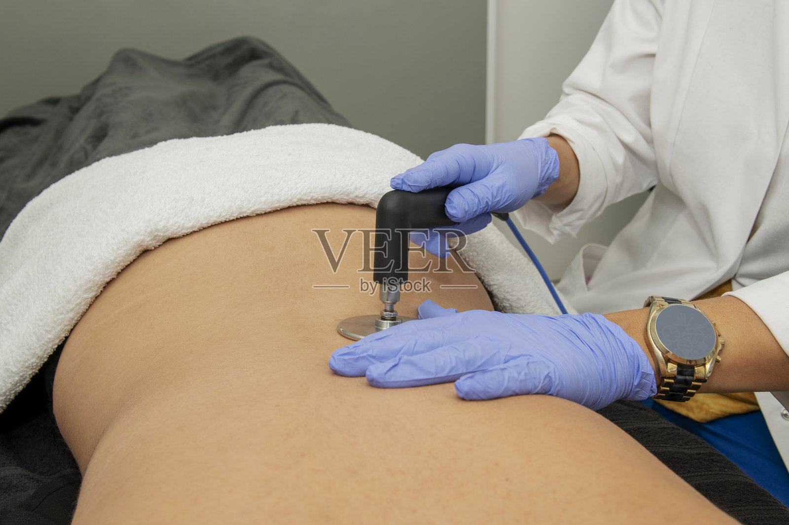 按摩师的手在患者背部进行物理治疗，使用用于皮肤美容治疗的电子设备照片摄影图片