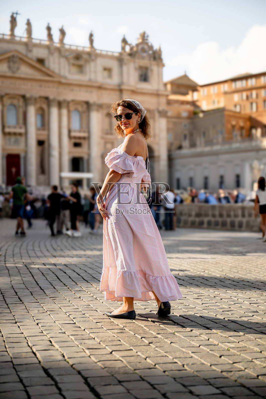 阳光下，身穿条纹连衣裙的女子走在城市广场上照片摄影图片