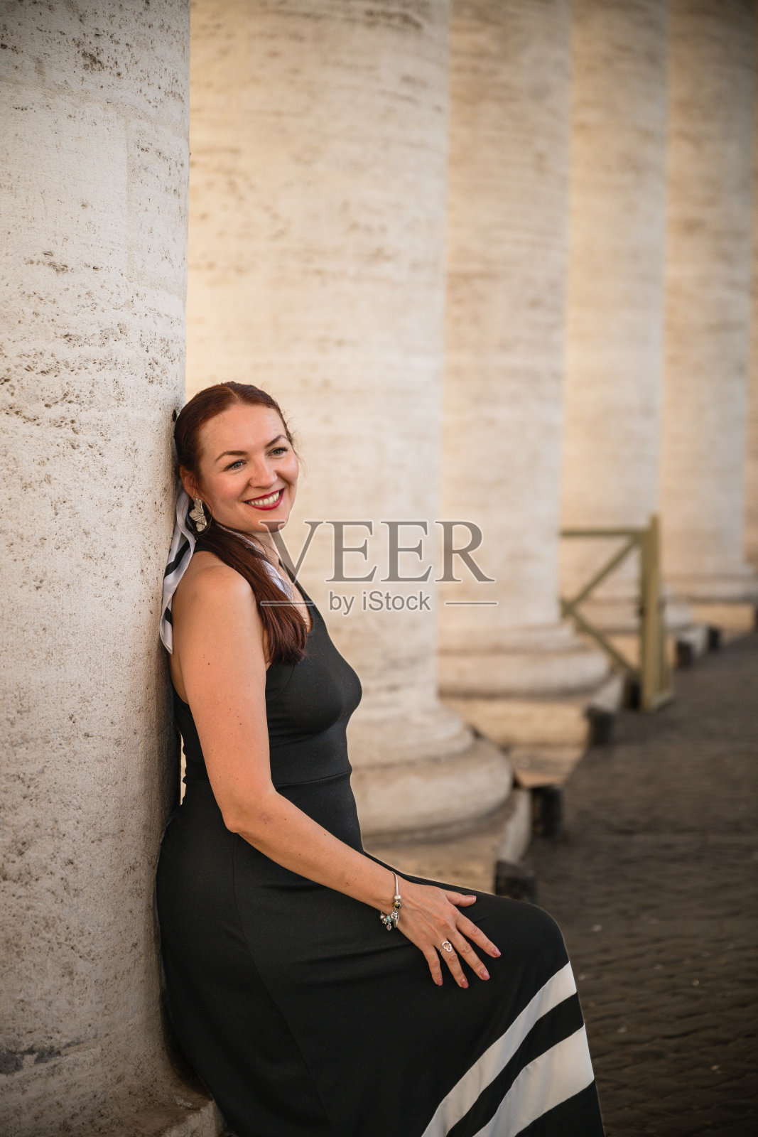 身着黑裙的女子站在阳光下的古老石柱旁照片摄影图片