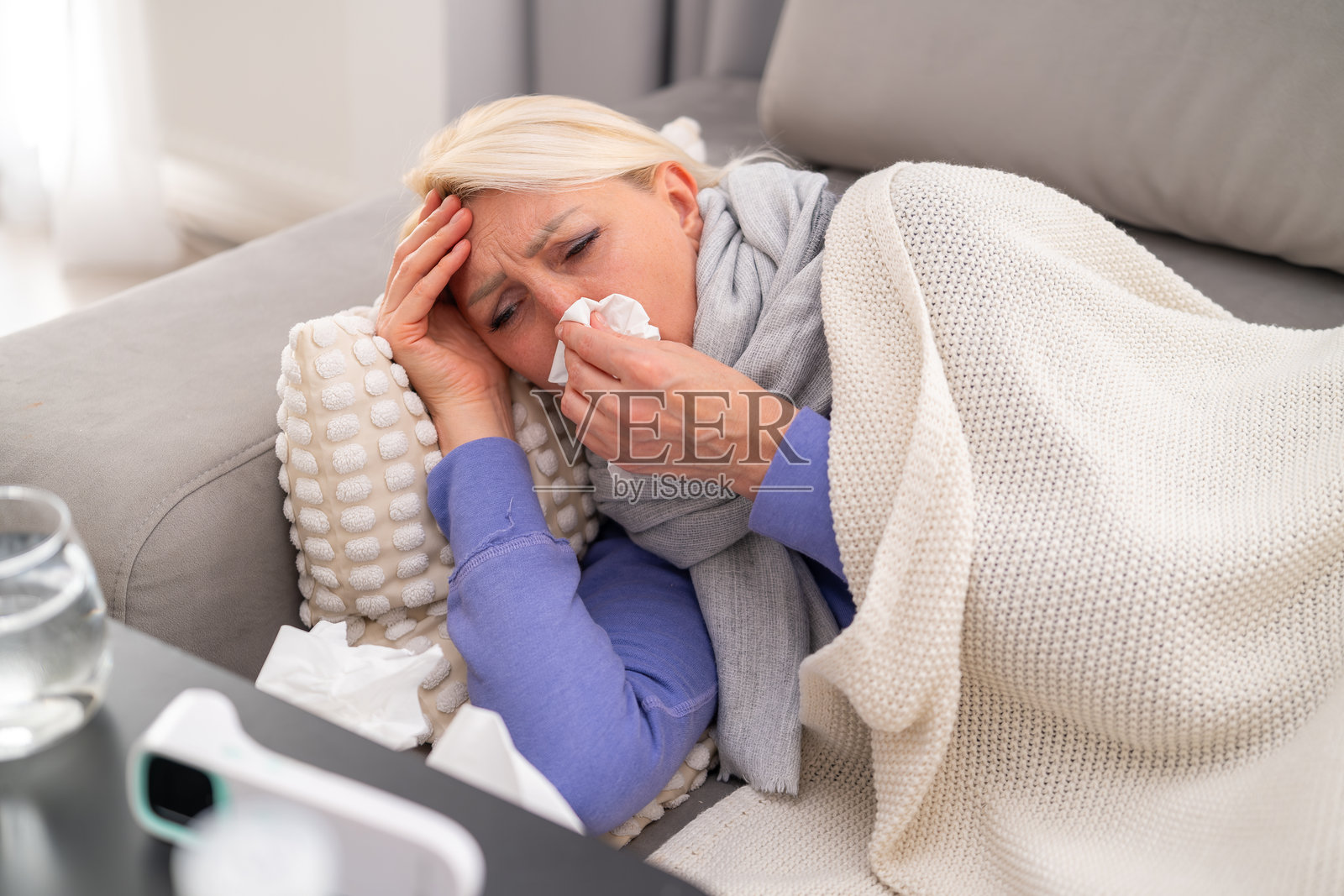 生病的女人躺在沙发上休息，旁边放着感冒药和体温计照片摄影图片