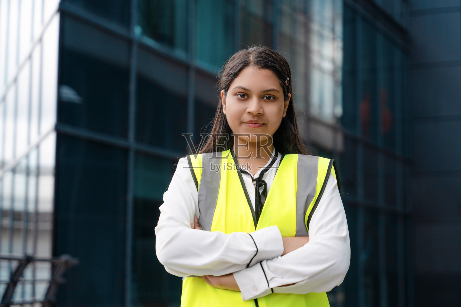 身穿安全背心的年轻女子，在现代办公楼前摆姿势照片摄影图片