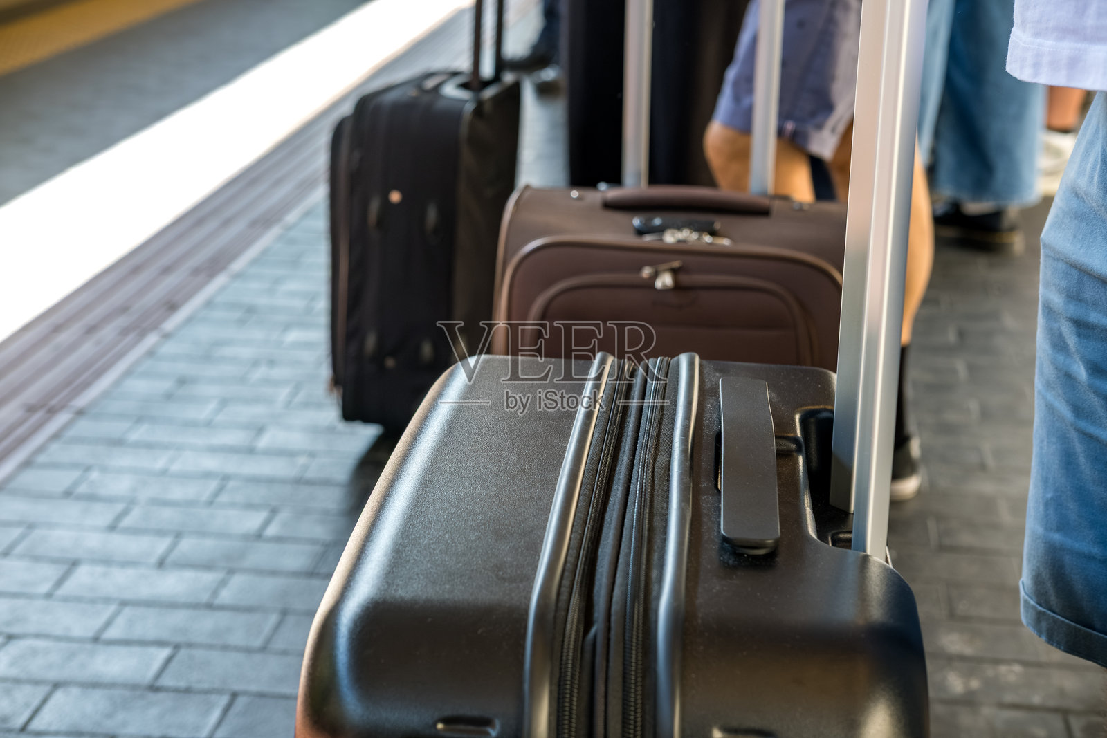 一位旅客带着黑色行李箱在火车站台候车，周围有其他乘客。照片摄影图片