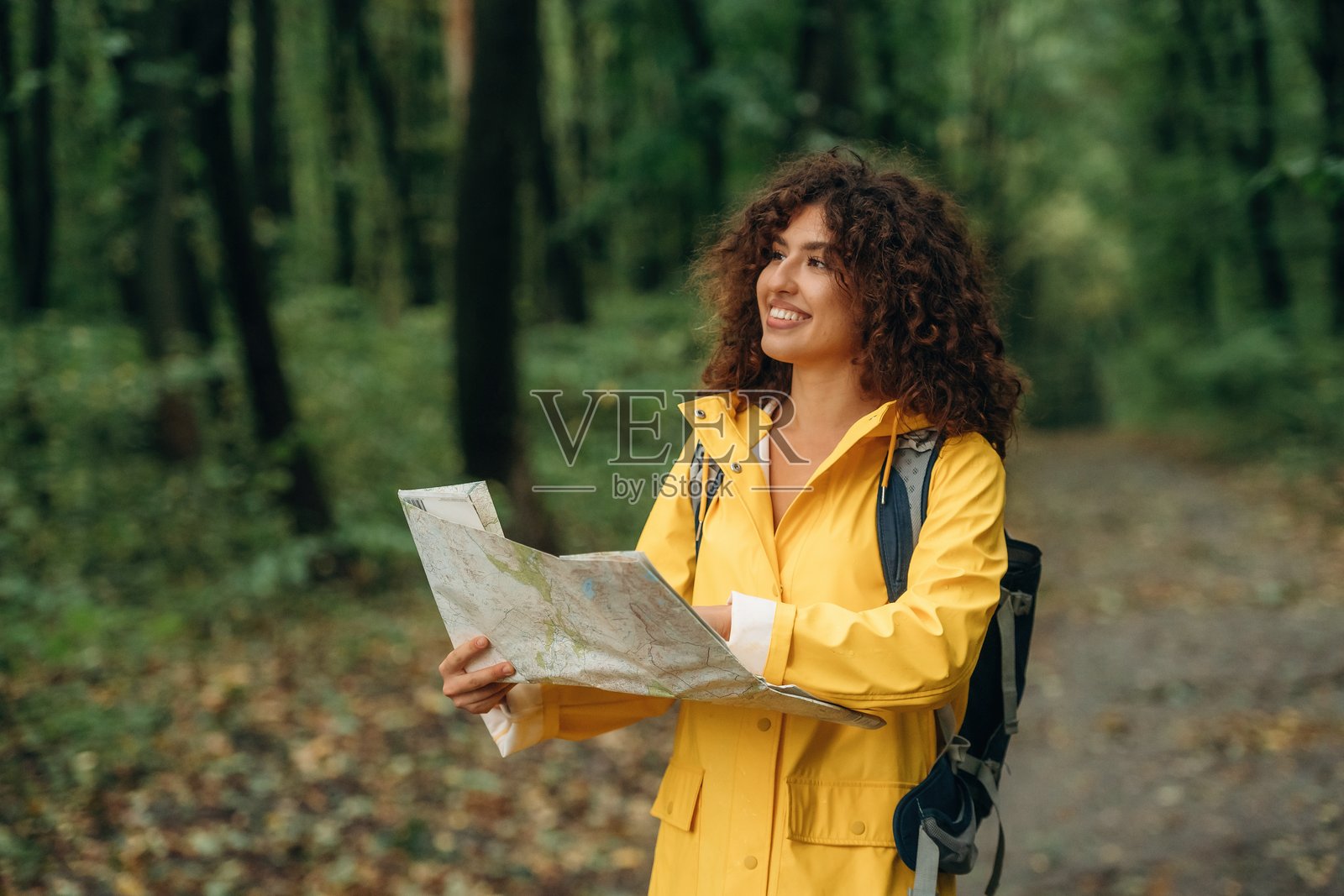 一只手拿着纸质地图，正在查看地点。一位年轻女子在雨中漫步于森林，享受自然。照片摄影图片