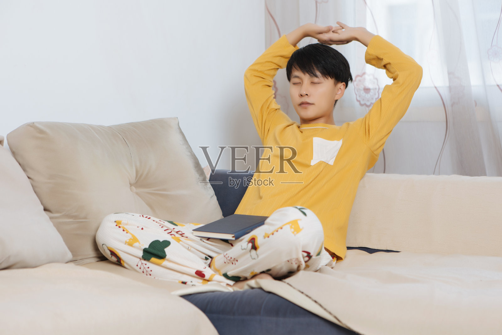 年轻的亚洲男性早晨坐在家中沙发上，伸展手臂和背部，享受个人健康和健康生活方式，在明亮的现代客厅中突出身体护理和室内休闲。照片摄影图片