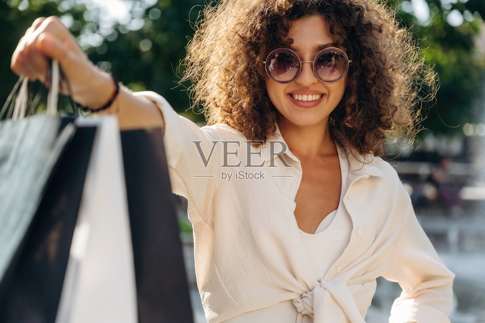 漂亮的快乐女人戴着太阳镜，提着购物袋走在城镇里照片摄影图片