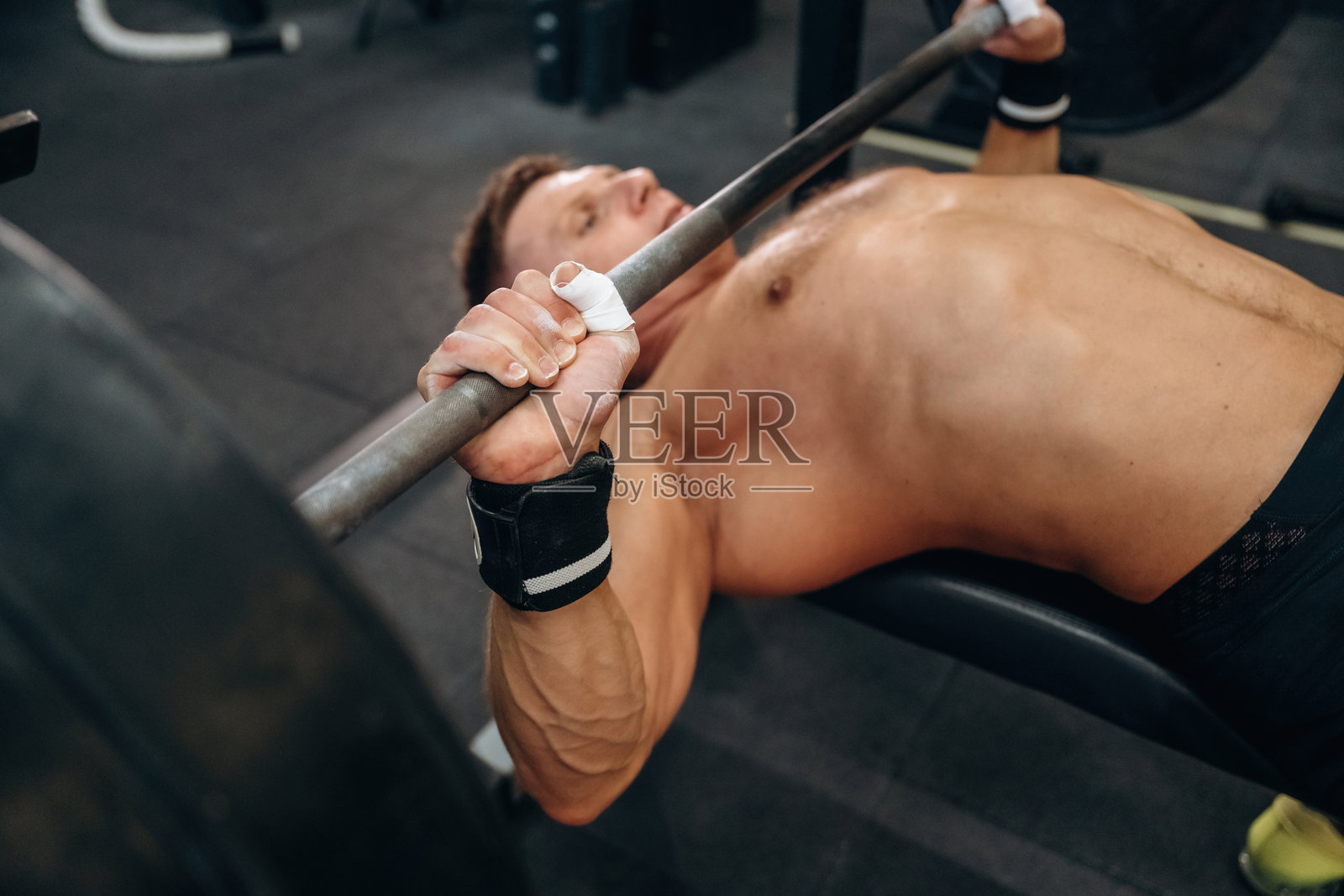 仰卧推举杠铃，运动型男子在健身房进行举重锻炼。照片摄影图片