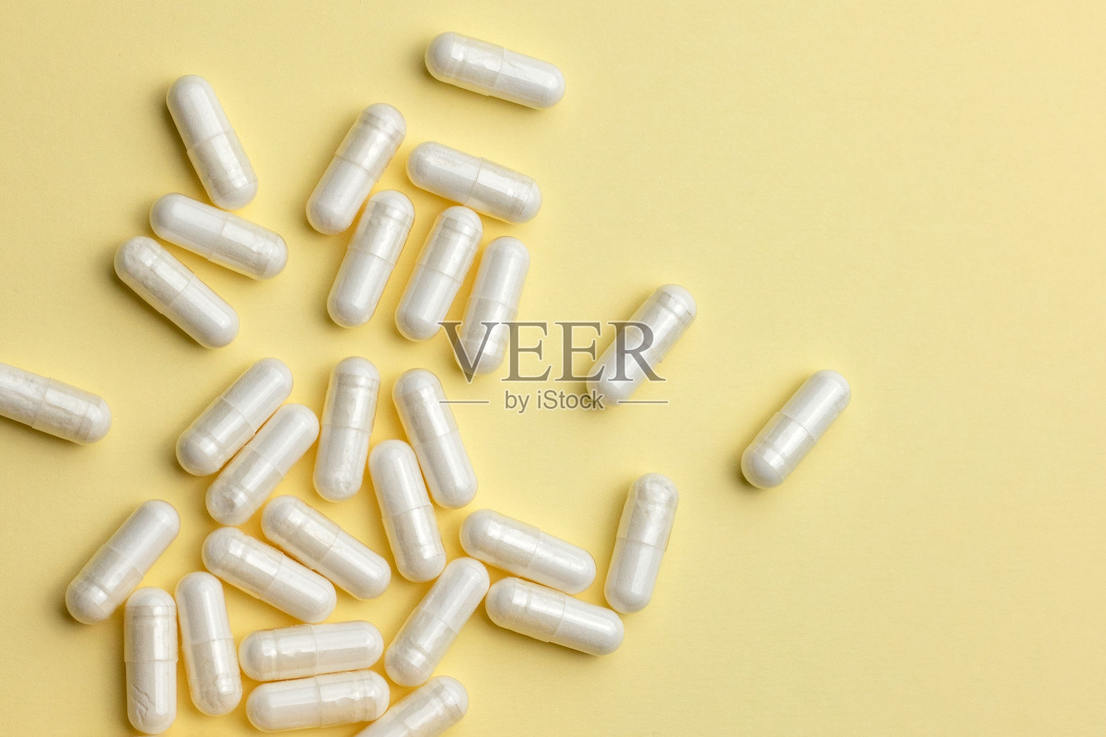 白色的药丸，里面装着药物、维生素或膳食补充剂，散落在浅黄色背景上。照片摄影图片