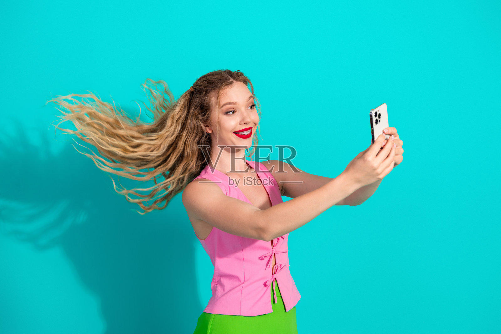 一位年轻女子身穿粉色上衣和绿色裙子，在绿松石色的背景前自拍，面带微笑，用于生活时尚广告拍摄。照片摄影图片