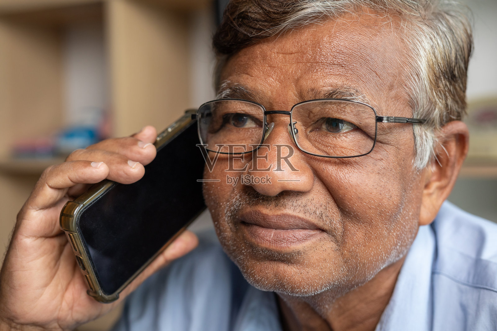 特写：一位年长的男士戴着眼镜，在家中放松地使用手机。人物与生活方式的概念。照片摄影图片