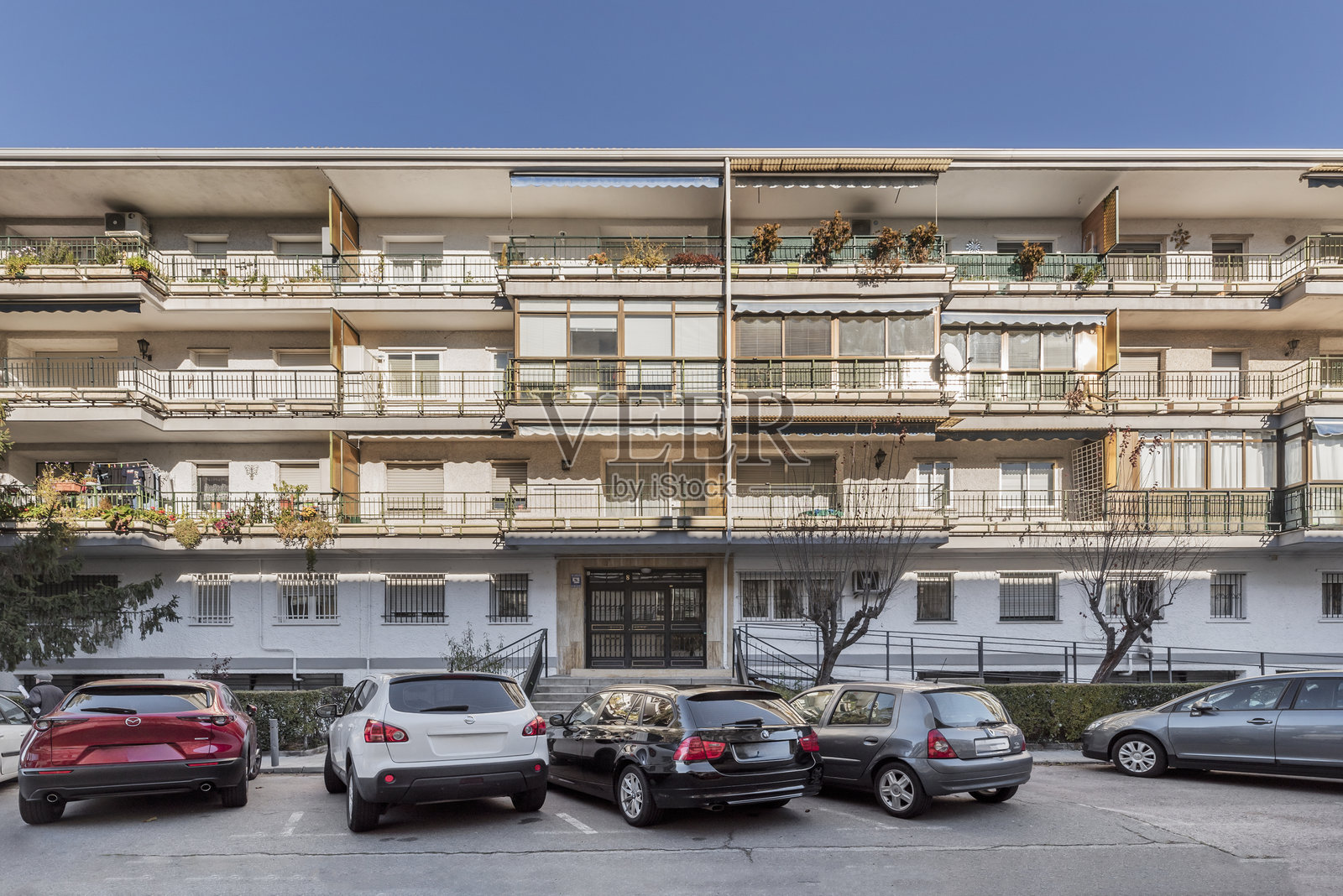 带花园、绿篱、树木和停放车辆的白色住宅楼，楼内有许多阳台照片摄影图片