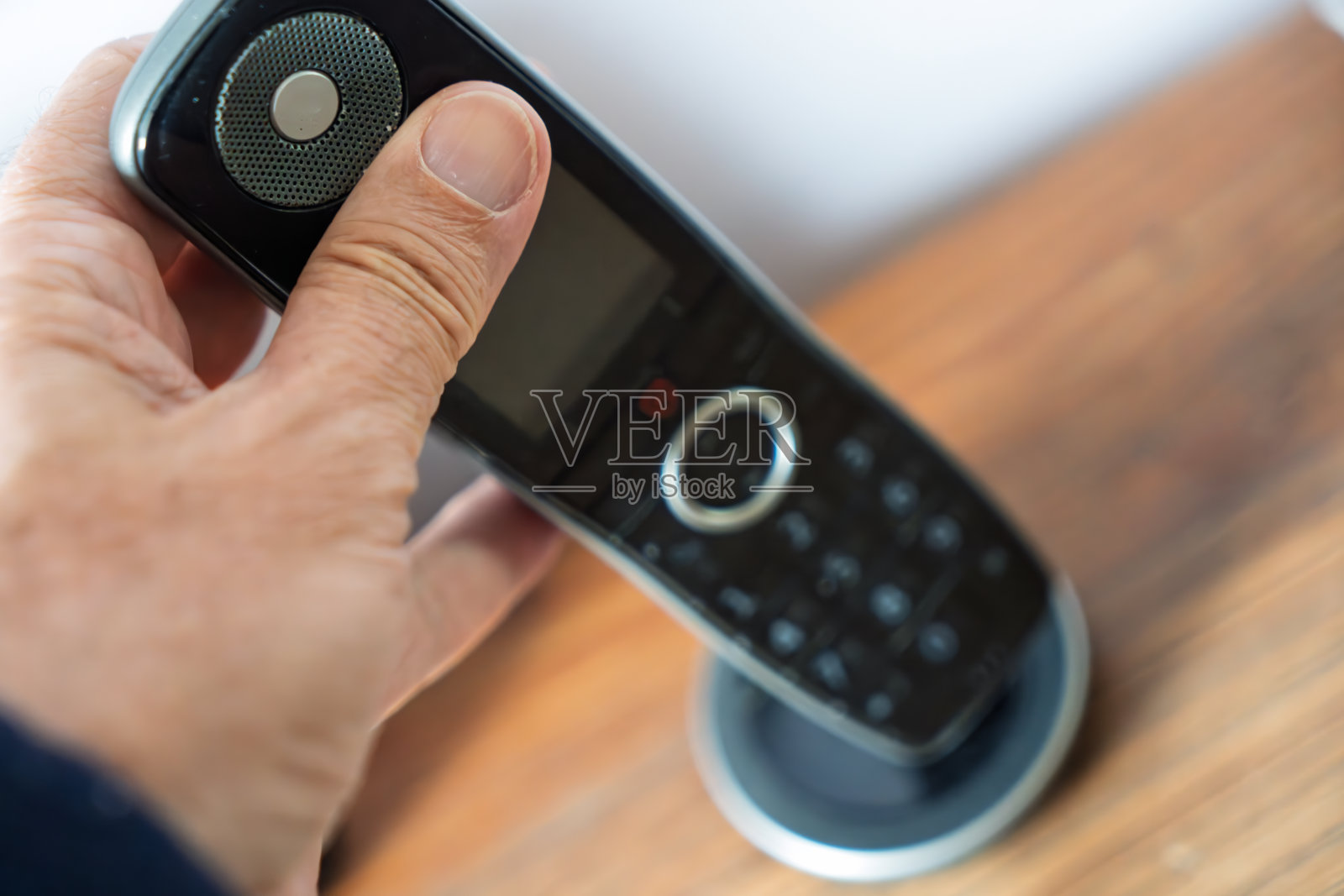 室内办公室场景中，男人的手握着一个放在木制办公桌上的黑色无绳电话照片摄影图片