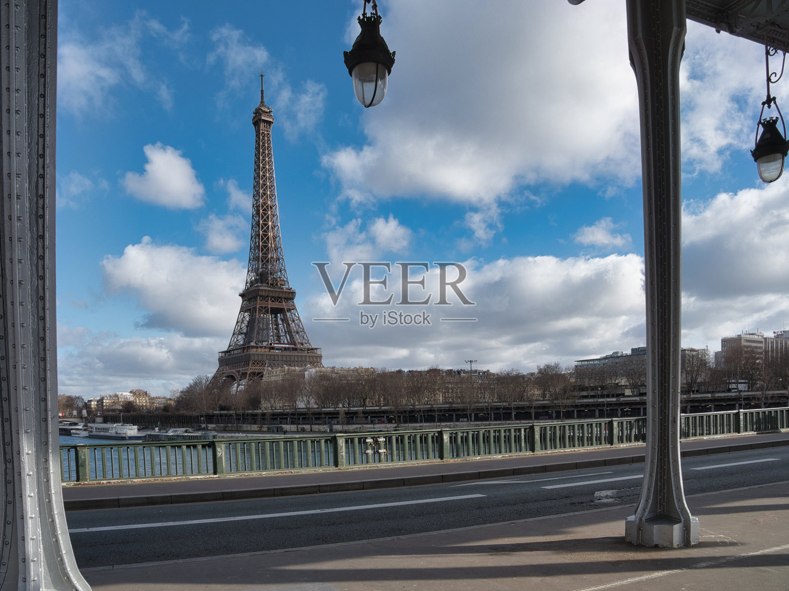 从比尔哈克姆桥上看埃菲尔铁塔 - 埃菲尔铁塔在晴朗的蓝天和白云下格外醒目，四周是巴黎比尔哈克姆桥的灰色金属结构和路灯。照片摄影图片