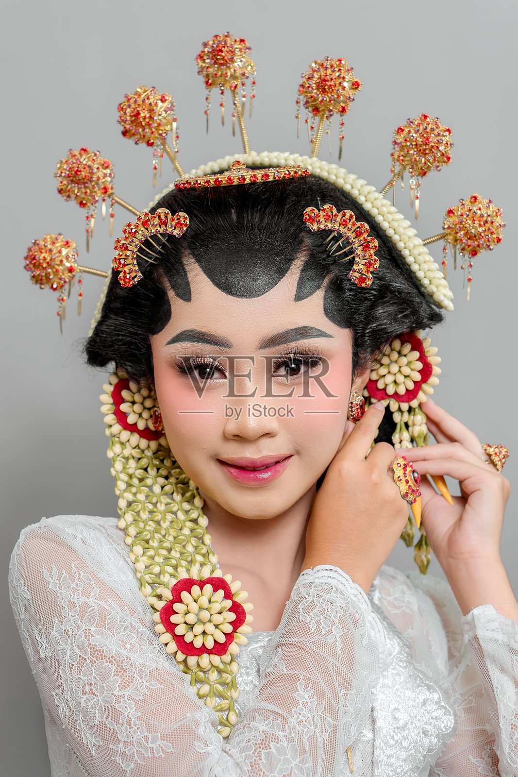 一位身着苏门答腊普特里传统服饰的印度尼西亚新娘，正在调整她的金色耳环。她戴着华丽的头饰，佩戴着茉莉花饰品，身穿蕾丝 kebaya，散发着优雅和魅力。照片摄影图片