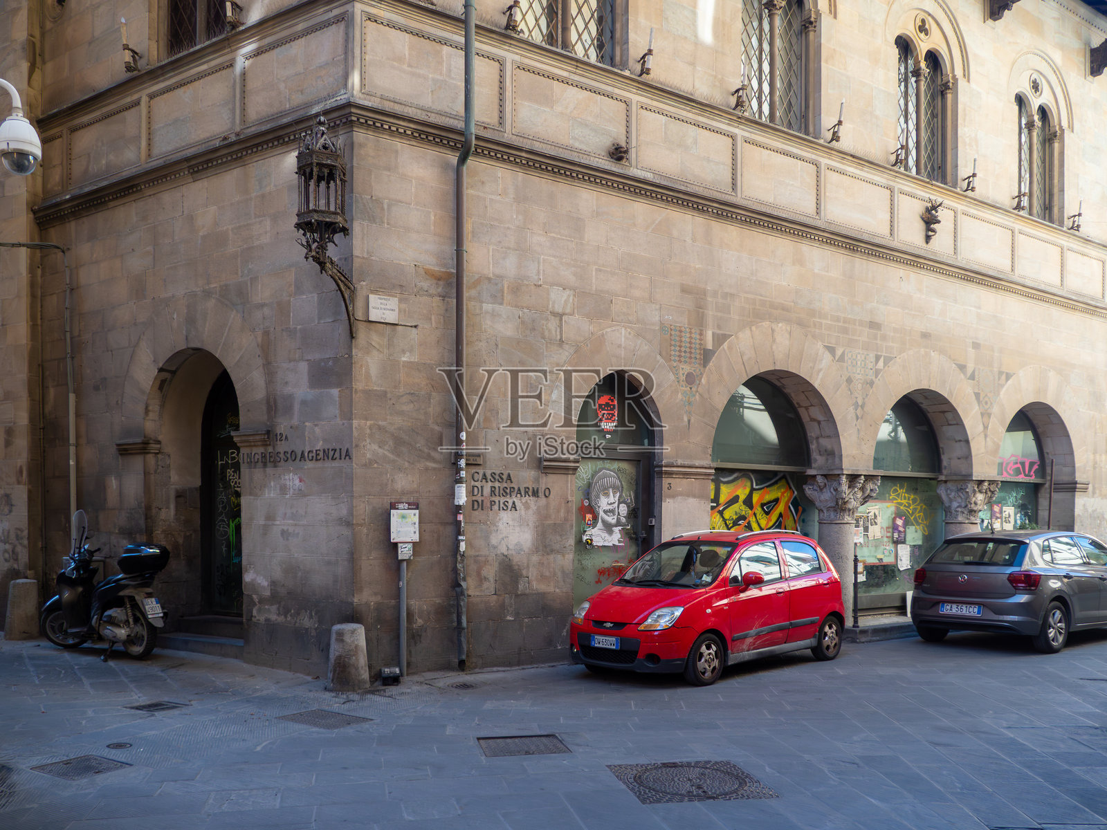 比萨街景，包含历史建筑、拱门、涂鸦、踏板车和停放的现代汽车照片摄影图片