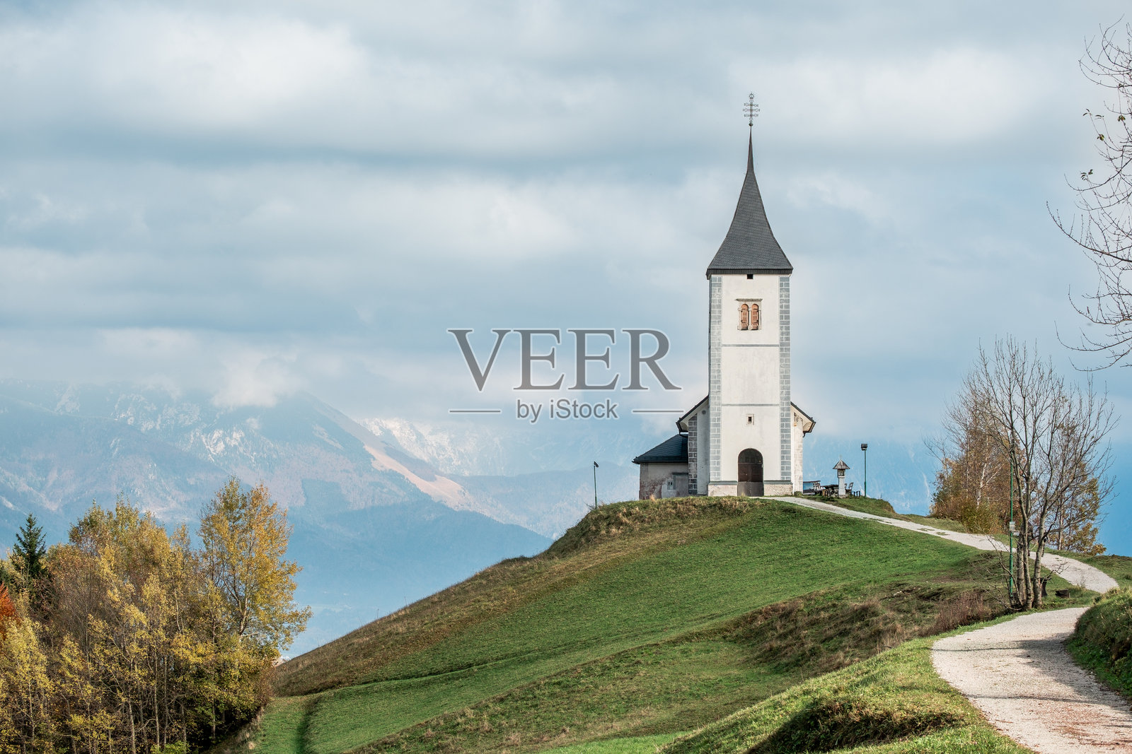 背景是山脉，教堂坐落在绿色的山丘上。照片摄影图片