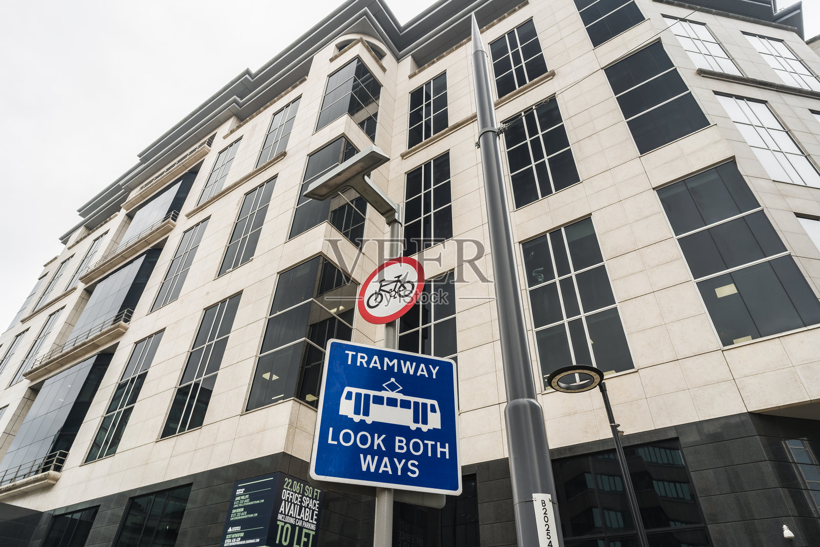 向上看，可以看到蓝色的电车轨道标志，背景中还有一栋办公楼。照片摄影图片