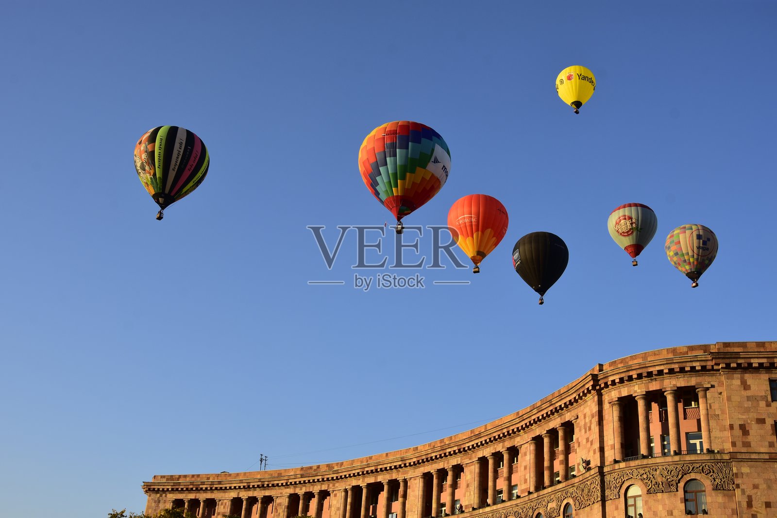 在市中心（共和国广场）举行了献礼城市日的七彩热气球启动仪式，画面展示了七个热气球和广场上建筑的部分外墙，时间为早晨。天空无云。照片摄影图片