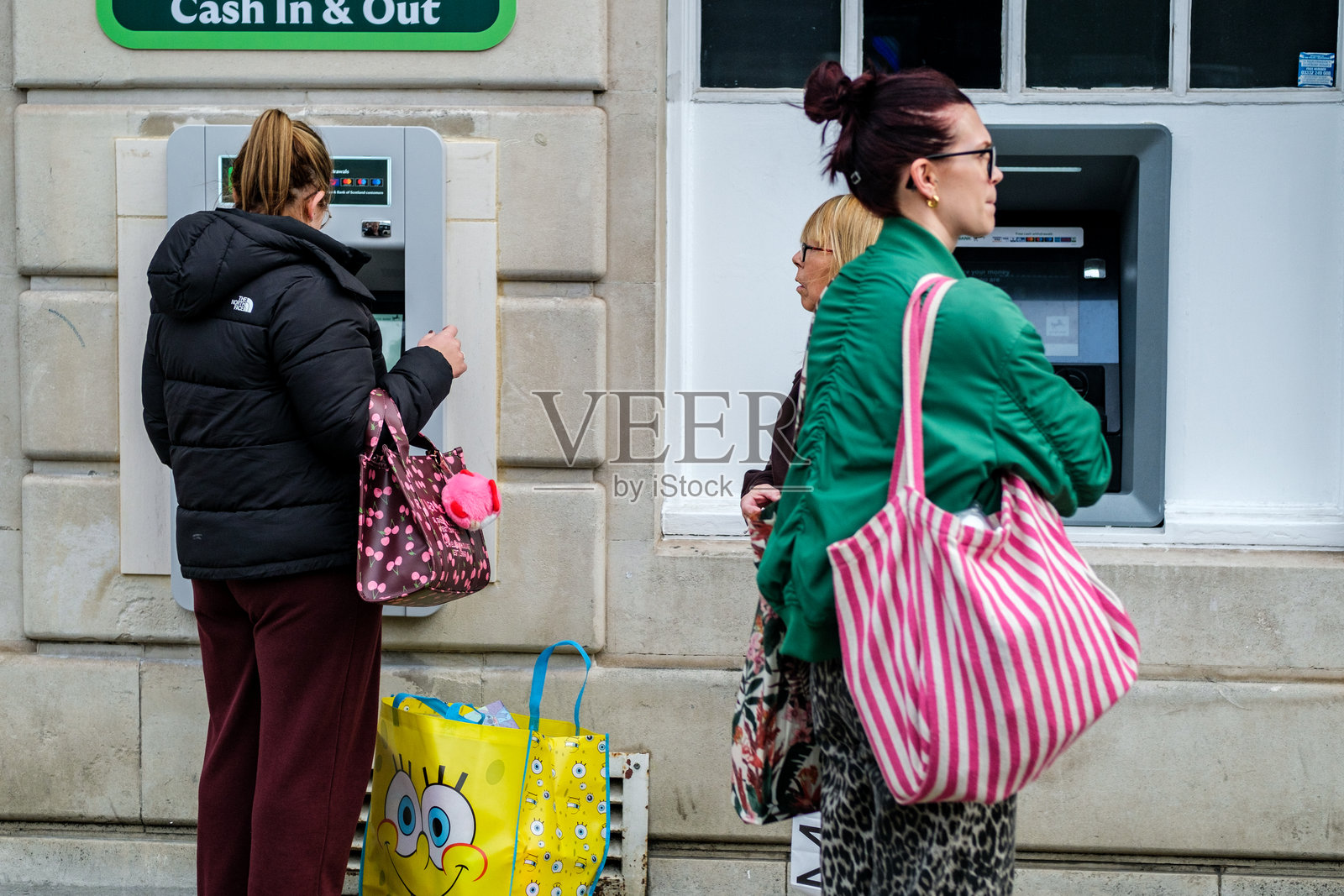 女性在 Lloyds 银行自动取款机前排队取款照片摄影图片