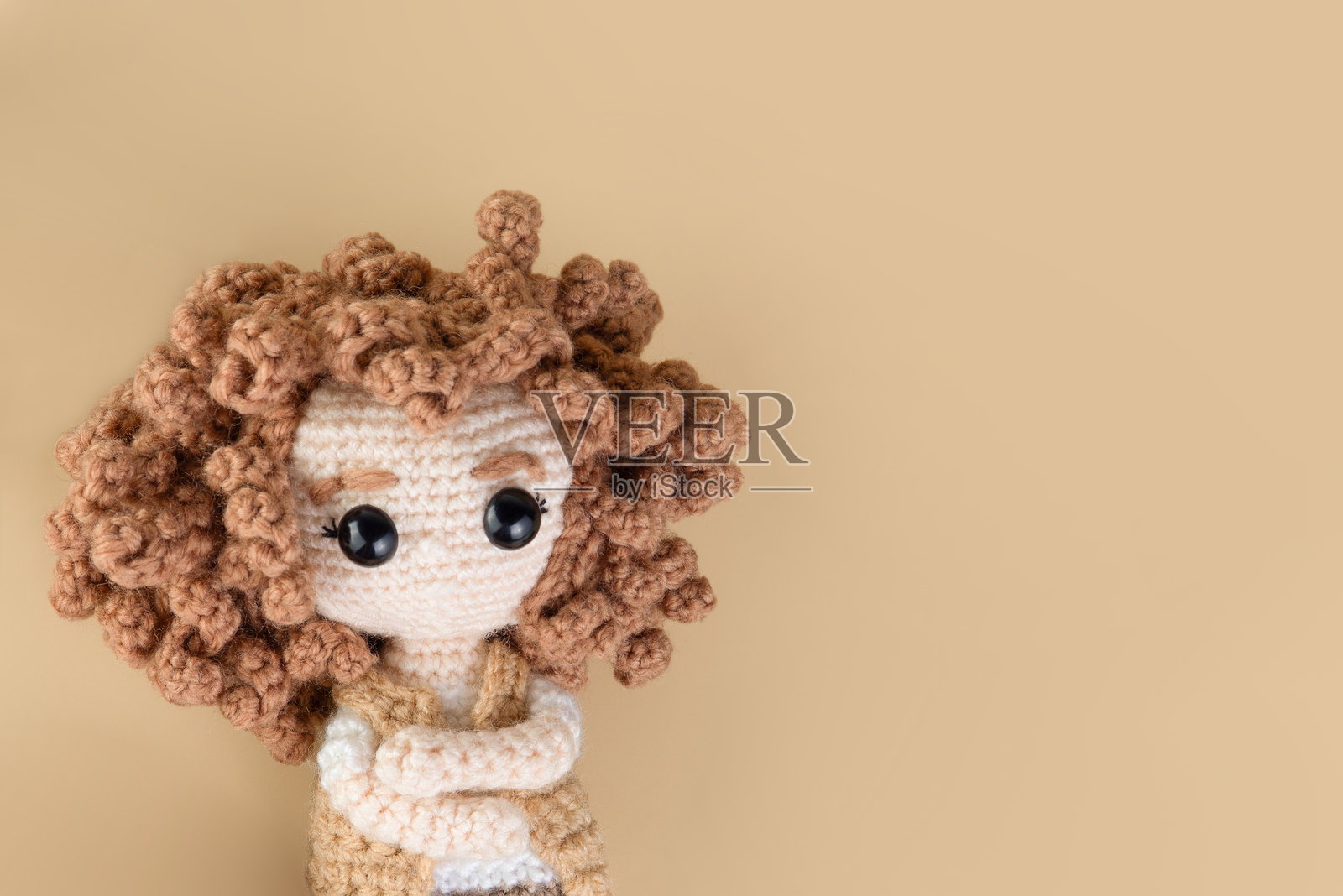 温暖背景下的可爱卷发针织玩偶肖像，极简构图。照片摄影图片