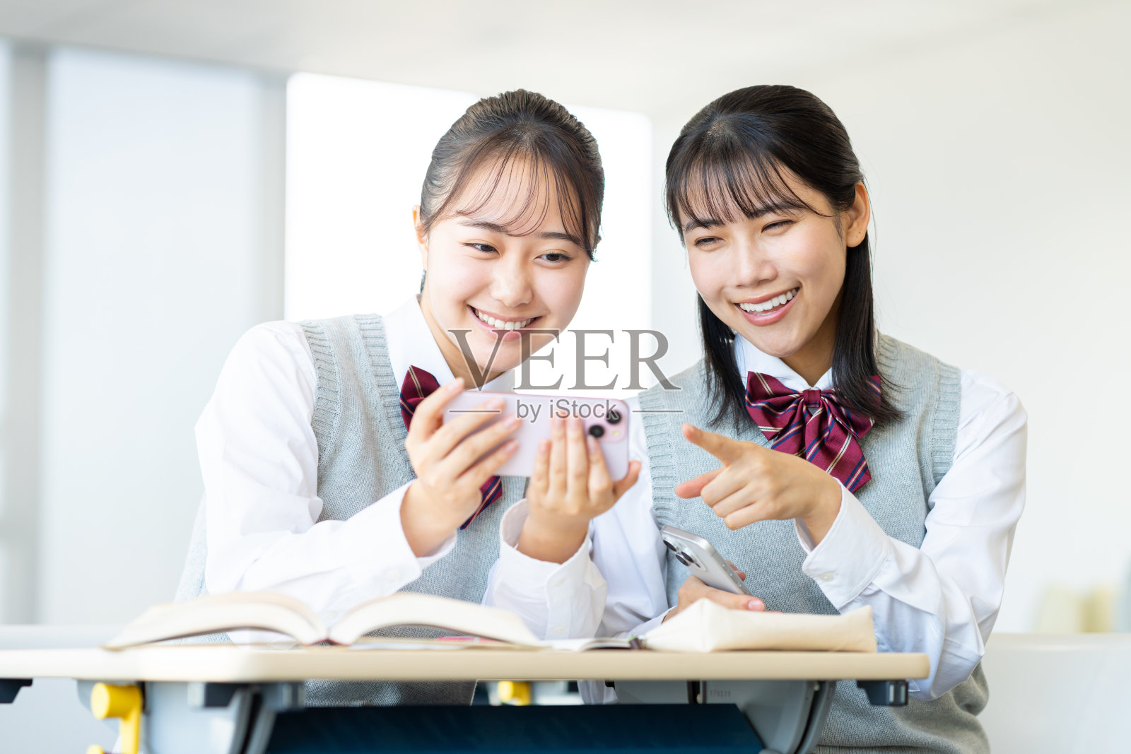 女高中生在教室里和朋友们一起看手机照片摄影图片