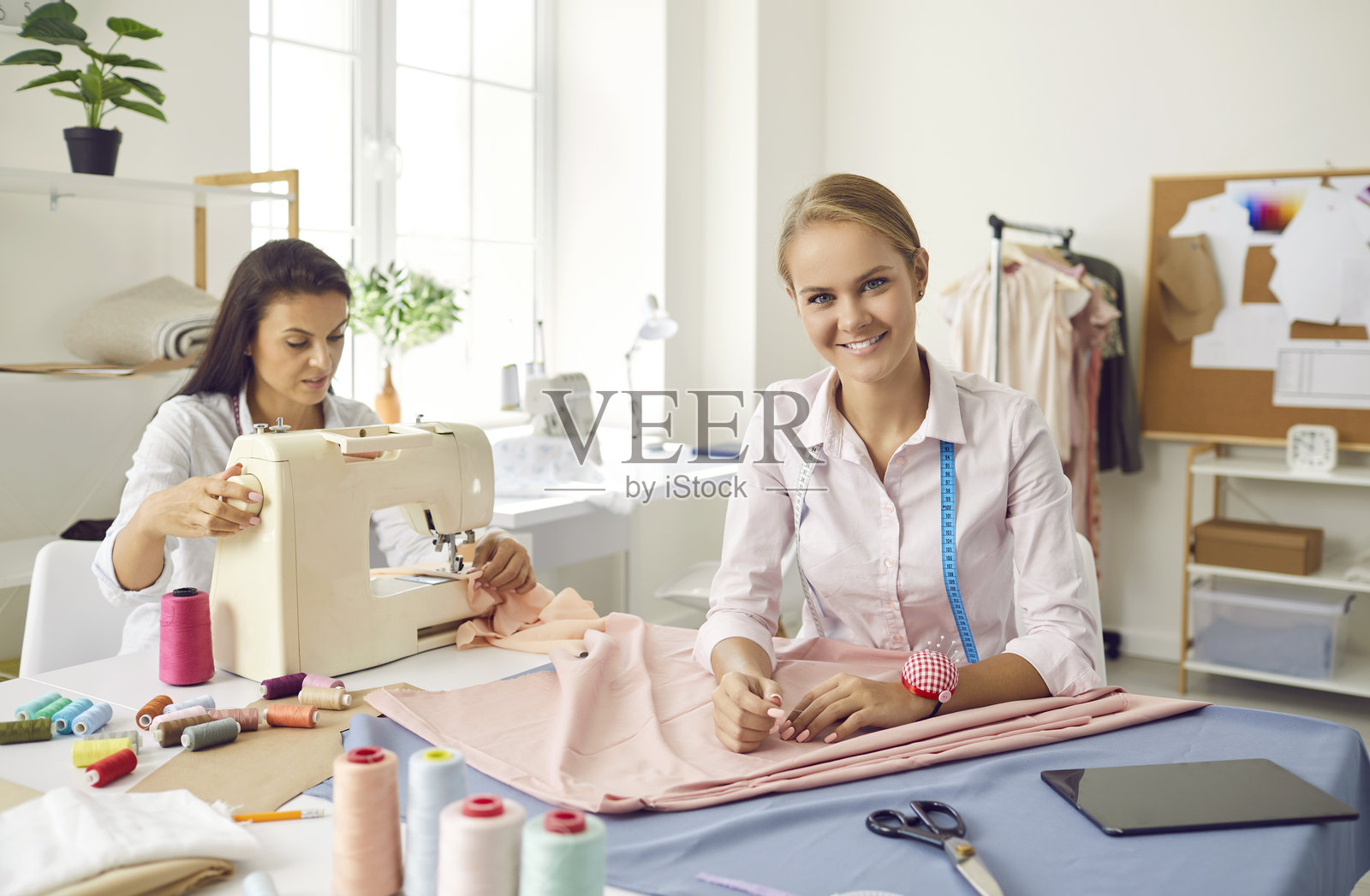 时装工作室里，一位面带微笑的设计师正在与布料打交道的肖像照片摄影图片