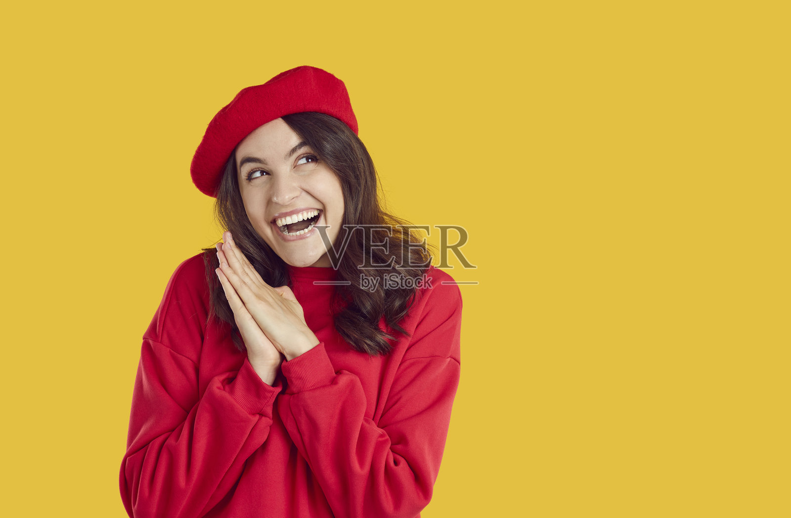 身穿红色贝雷帽和运动衫的漂亮快乐的棕发女子，在黄色背景上看向别处。照片摄影图片