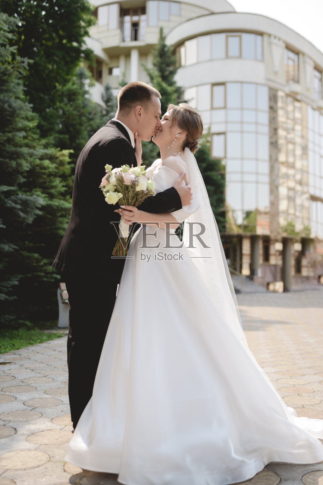 一对幸福的新婚夫妇手牵着手，在结婚当天漫步于城市之中。这对恩爱的恋人正在拍摄婚纱照。照片摄影图片