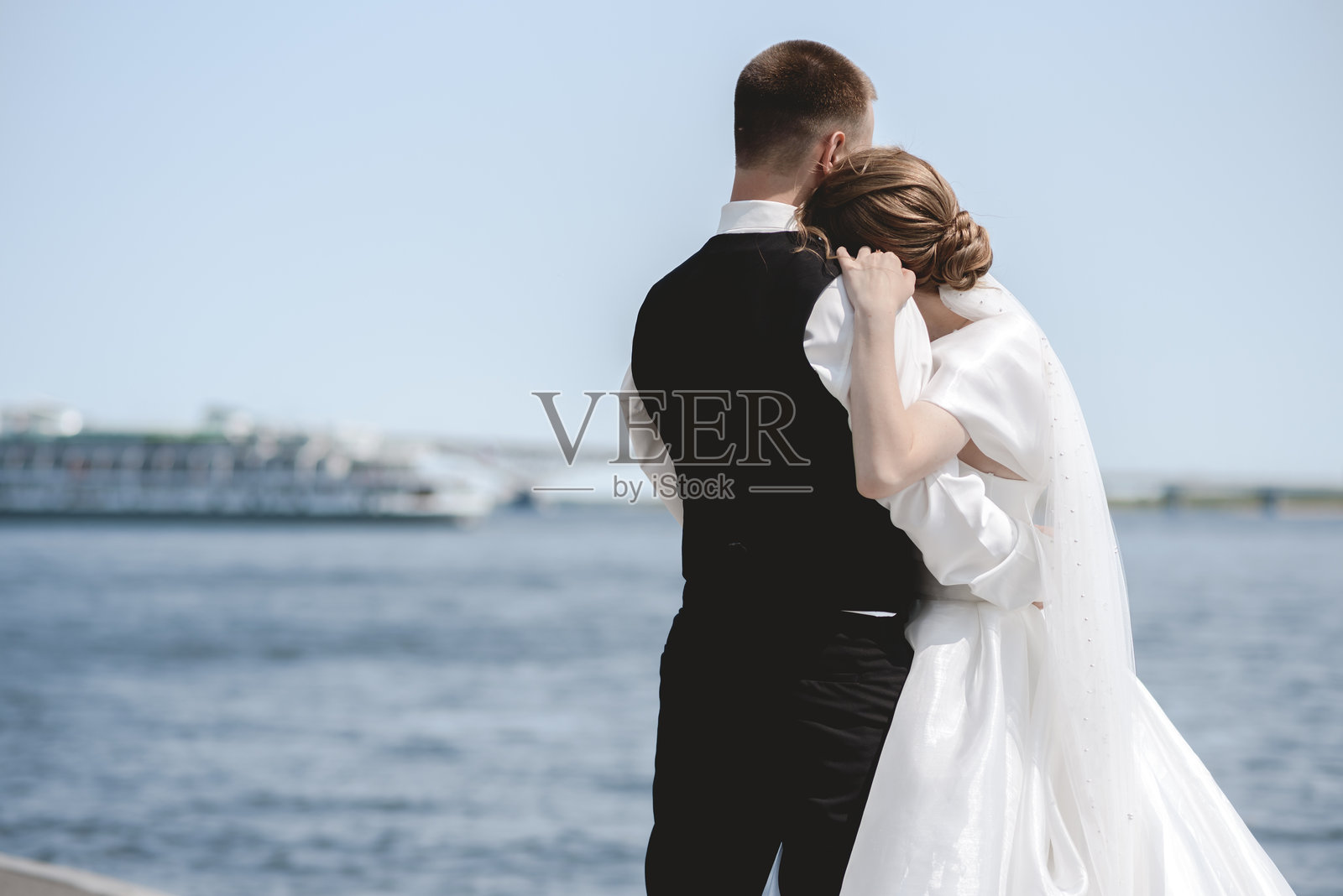 一对快乐、充满感情的新婚夫妇在拥抱。一位快乐的新娘和时尚的新郎手牵着手，在城市中漫步。照片摄影图片