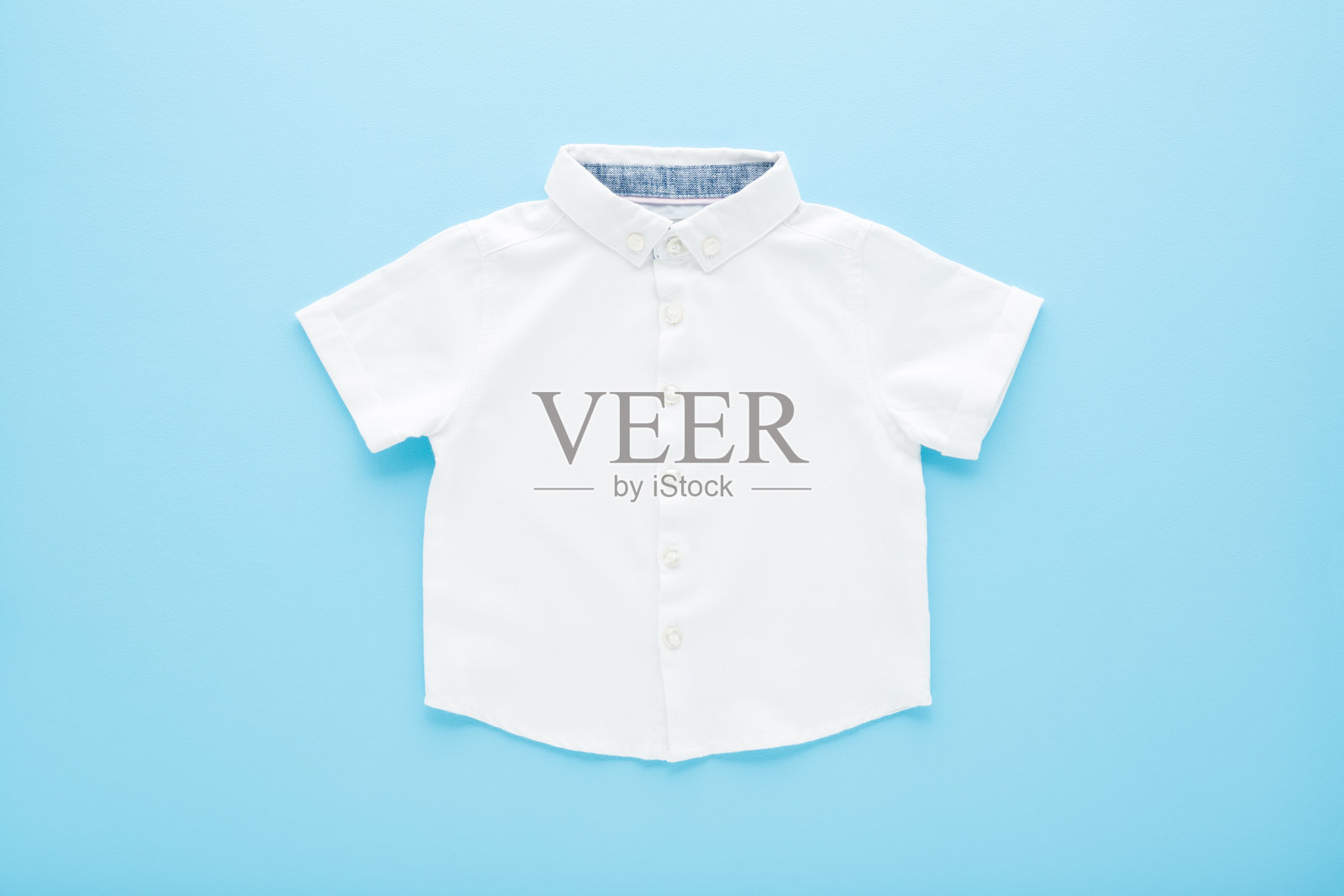 熨烫过的白色经典衬衫，置于浅蓝色桌子背景上。柔和色彩。特写。适合小男孩的衣服。俯视角度。照片摄影图片