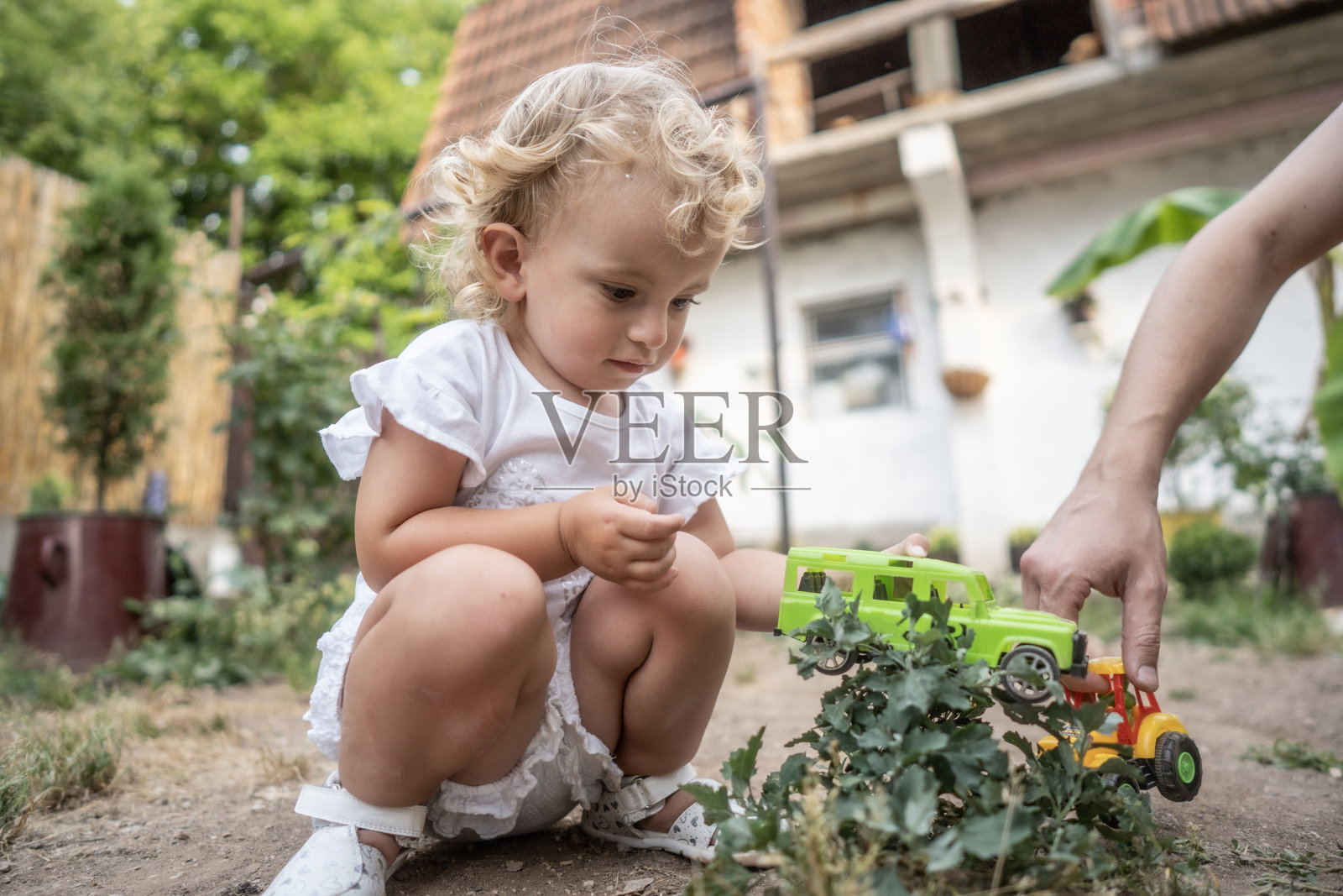小女孩在花园家院里玩亮闪闪的玩具卡车，有成年人帮忙照片摄影图片