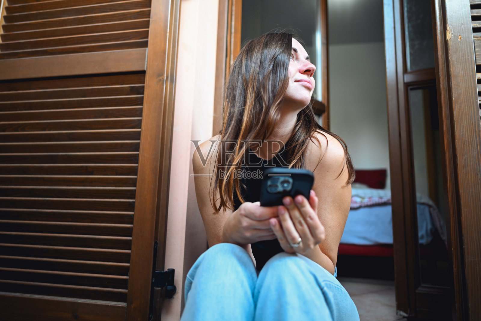 年轻女子坐在门框里，微笑着看向别处，手中拿着一部智能手机照片摄影图片