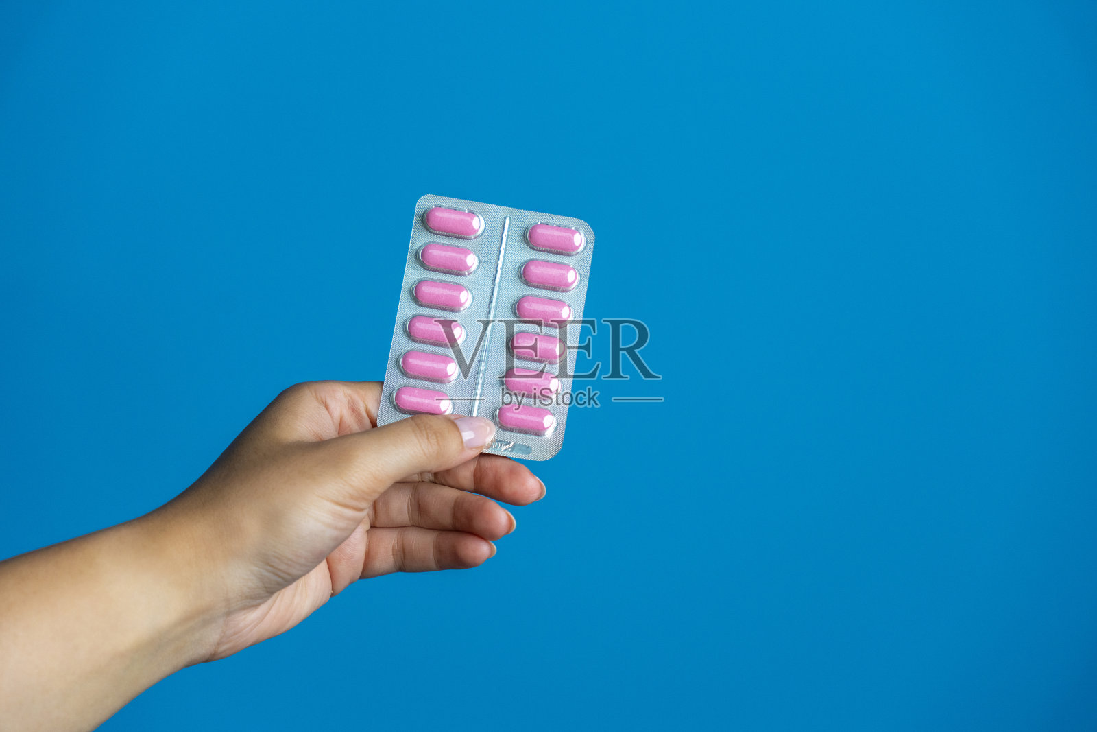 蓝底上手持粉色药丸泡罩包装的双手照片摄影图片