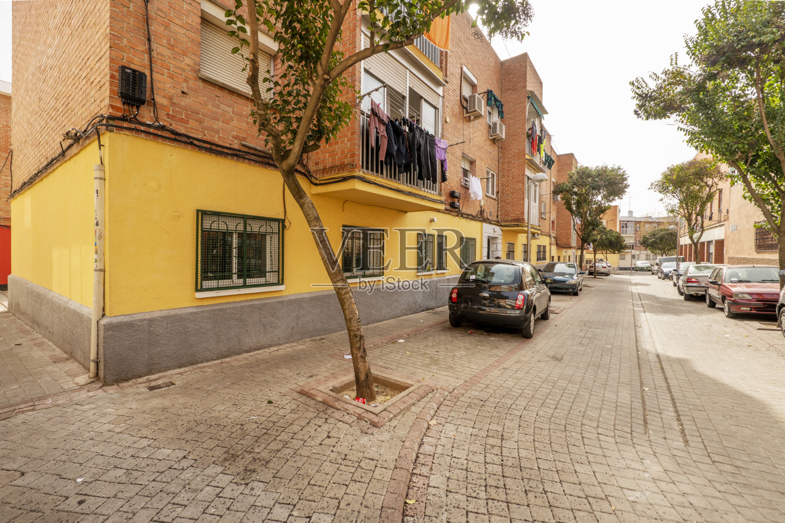 三层砖砌外墙的住宅楼，门前有鹅卵石街道和树木围栏照片摄影图片