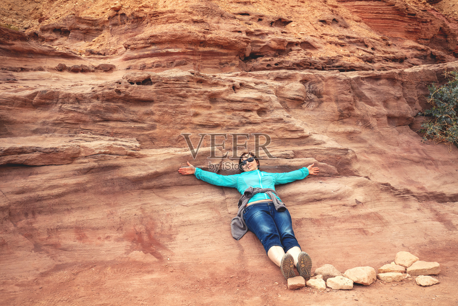 年轻的女游客躺在沙漠干涸河床的红峡谷中。位于以色列内盖夫沙漠的红峡谷。照片摄影图片
