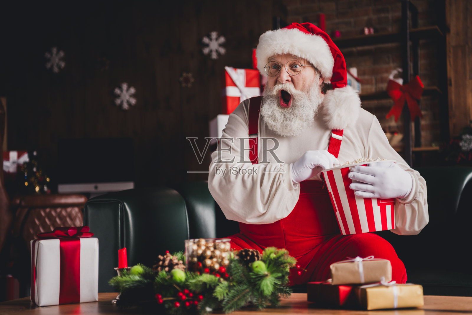 圣诞老人手捧条纹爆米花桶带来惊喜，爷爷在节日的礼物和温馨的家居装饰旁开怀大笑，共享欢乐圣诞时刻照片摄影图片