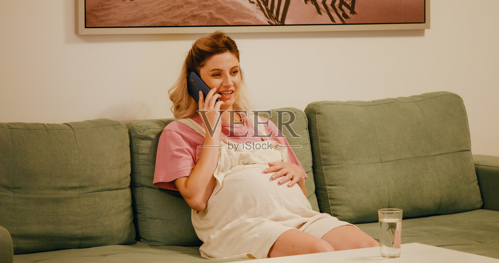 沙发上，一位微笑的孕妇正在用智能手机通话。照片摄影图片