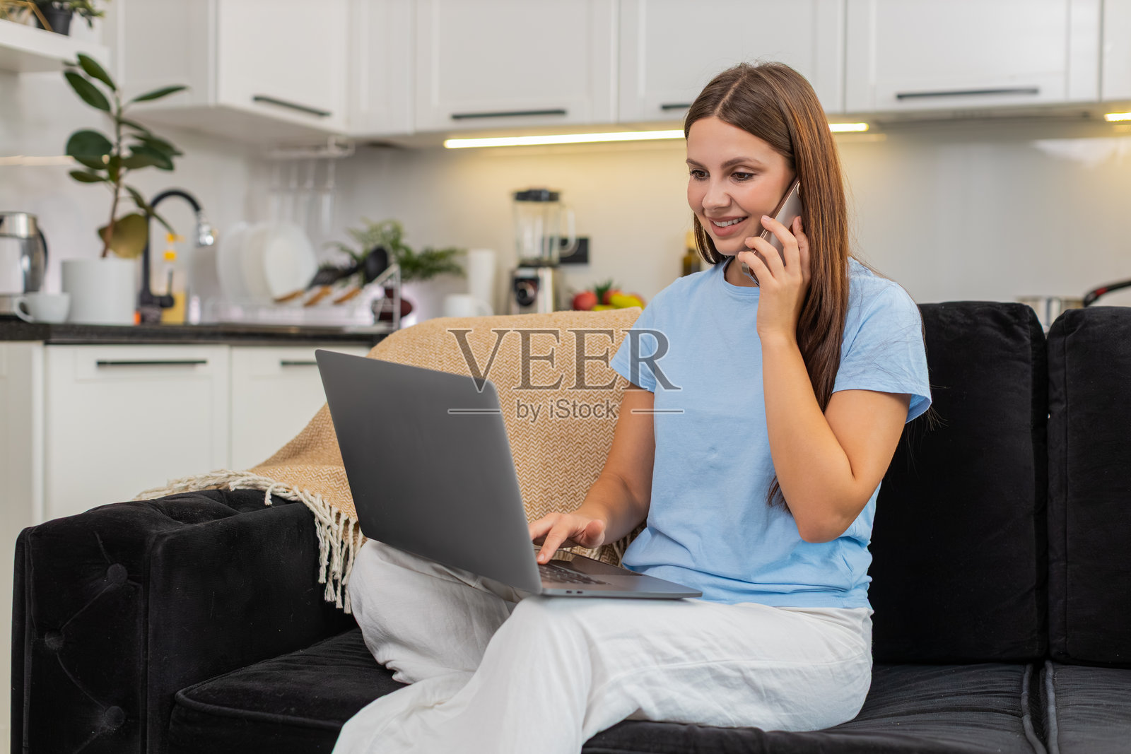 年轻女子专注于使用笔记本电脑并接听智能手机，展现多任务处理能力并处理客户事务。照片摄影图片