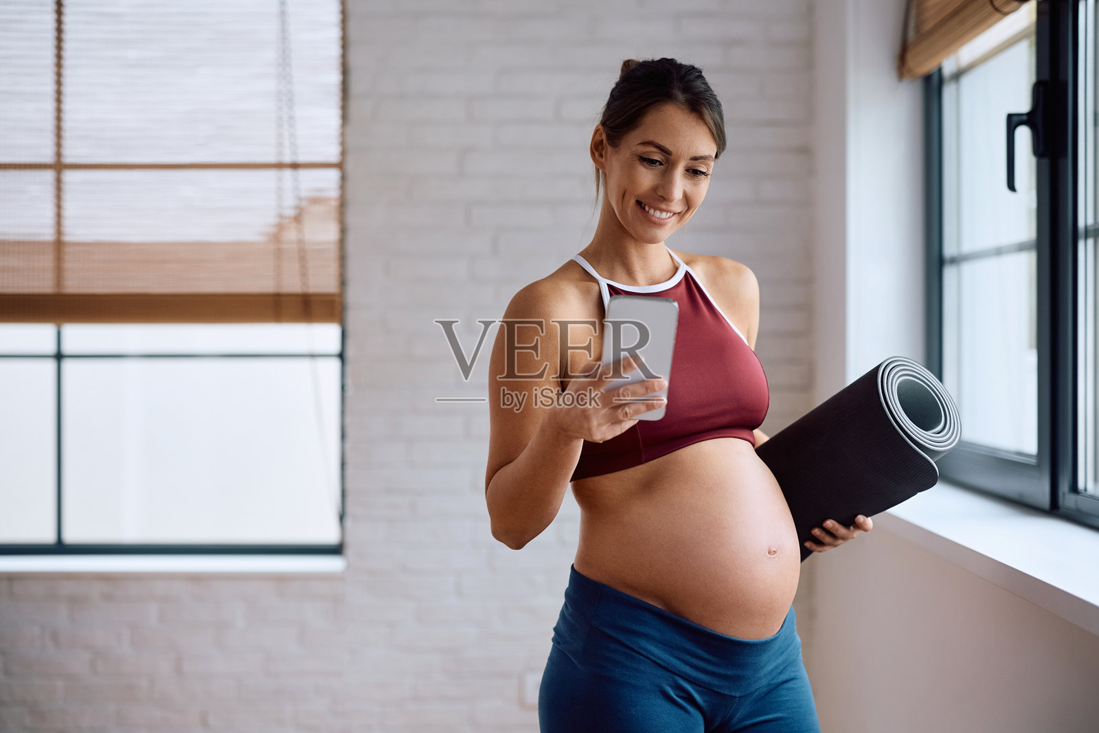 快乐的准妈妈在瑜伽馆健身时使用手机上的应用程序照片摄影图片