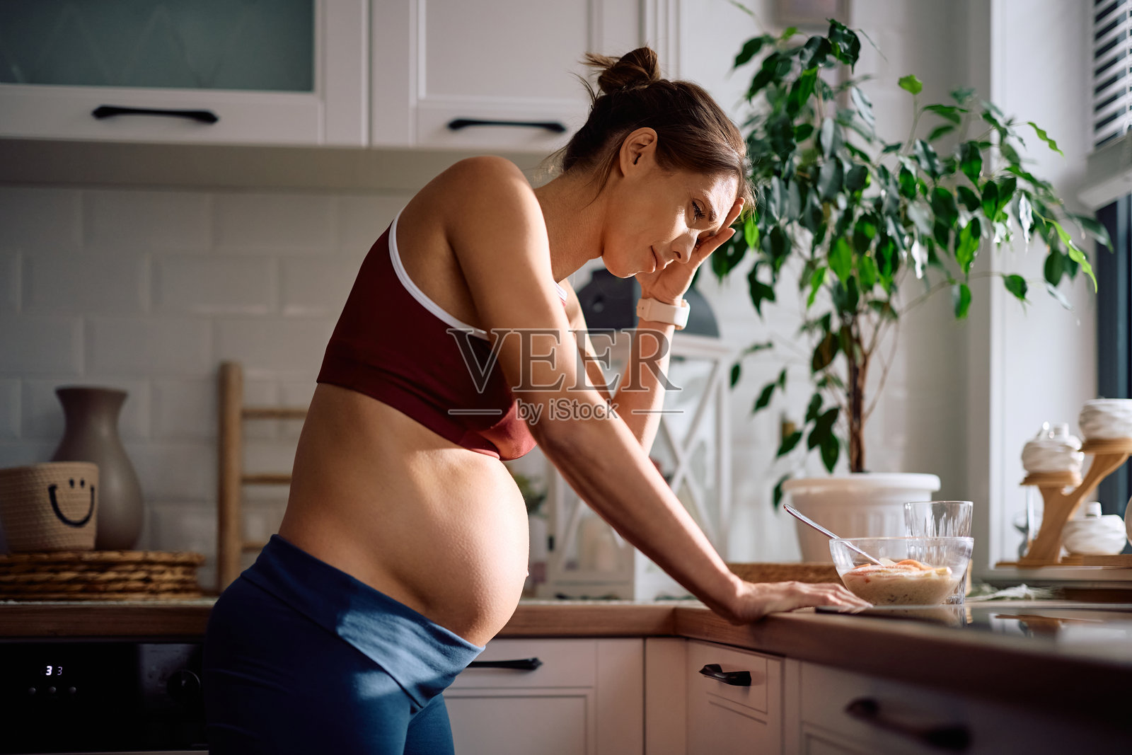 一位心烦意乱的孕妇在厨房里头痛。照片摄影图片