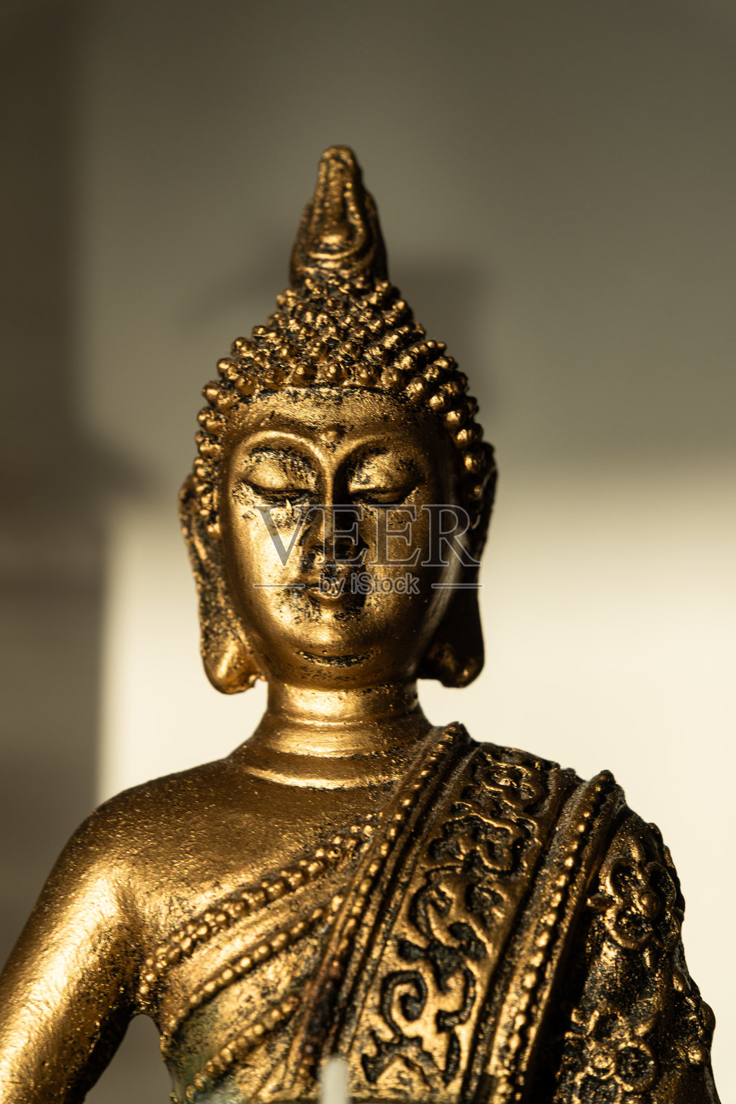 一尊金色的佛像，手持烛台和白色蜡烛，呈冥想坐姿，背景为米色，带有阴影。照片摄影图片