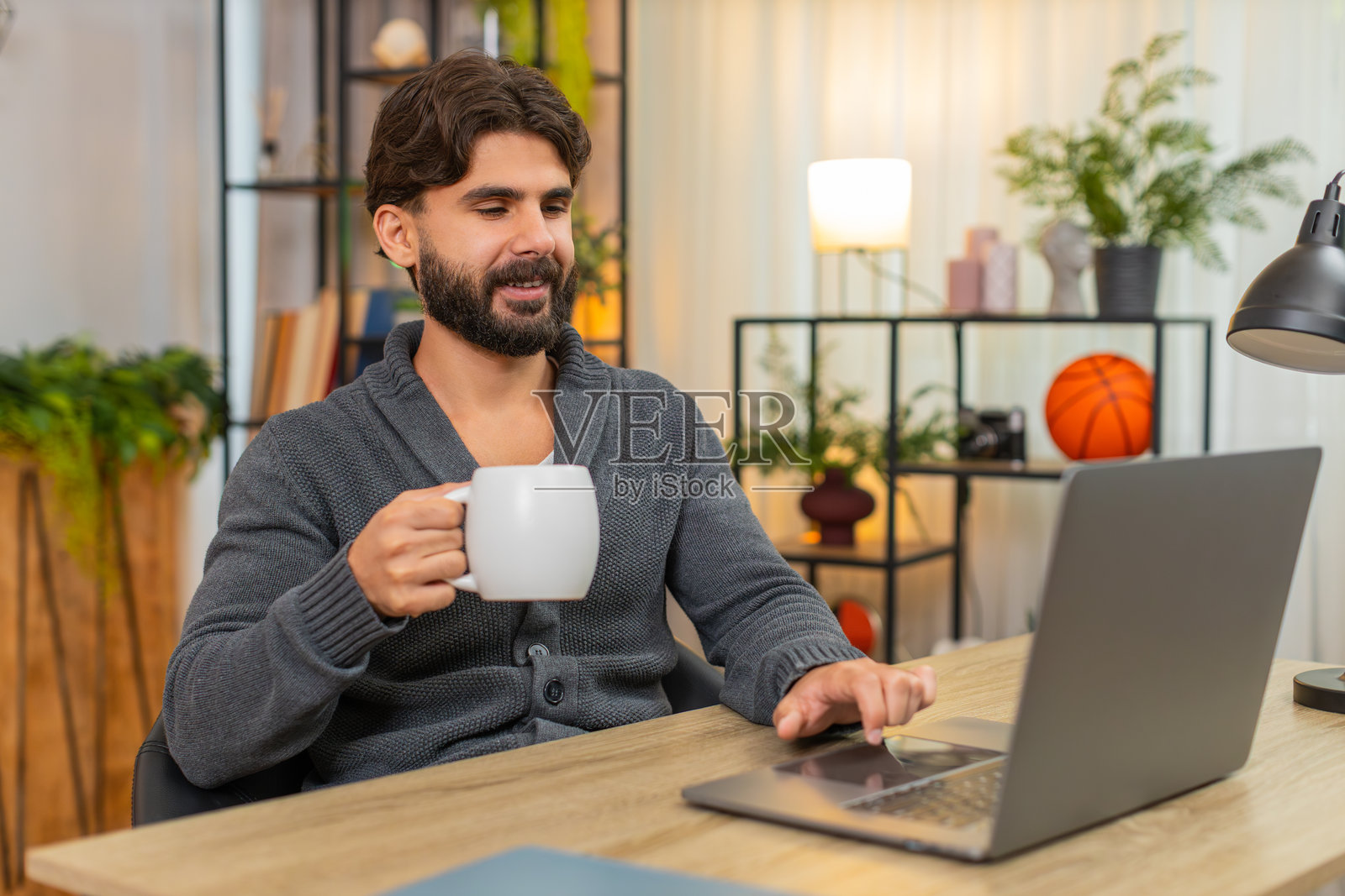 印度男人在笔记本电脑前喝咖啡或茶，查看待办事项清单，标记已完成，并竖起大拇指，表现出积极的喜悦。照片摄影图片