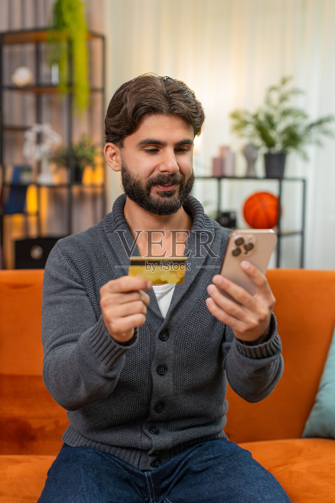 印度男子用智能手机完成在线购买，输入CVV，付款获批准，满意地笑着说太棒了照片摄影图片