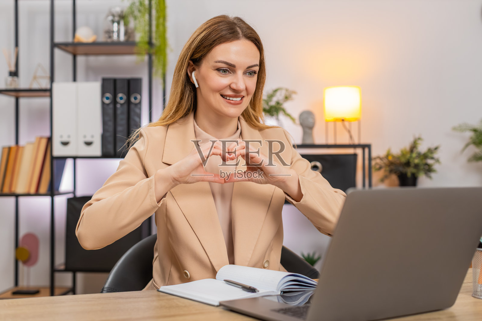 女商人在戴着耳机的视频通话中听到表扬，开心地笑了，表示感谢并做出心形手势，然后写下下一步计划。照片摄影图片